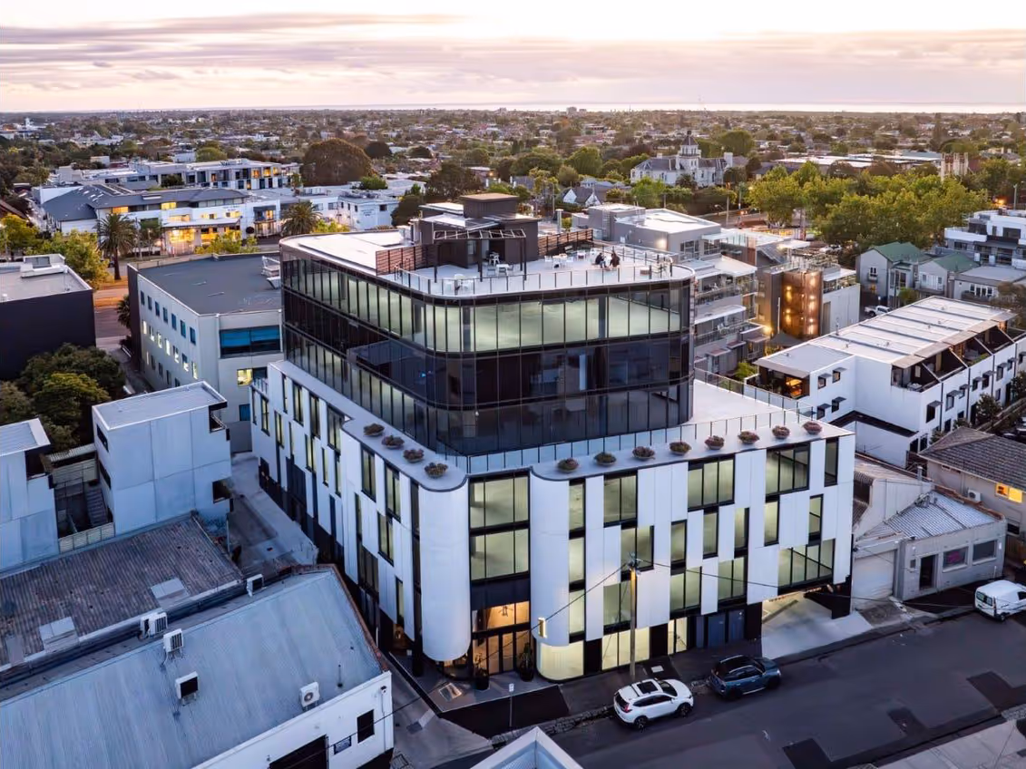 Aerial view of a modern multi-story building with white and black exterior in an urban neighborhood at sunset.