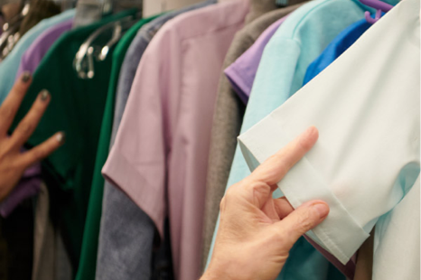 A hand reaches toward a rack of hanging garments in green, purple, and light blue.