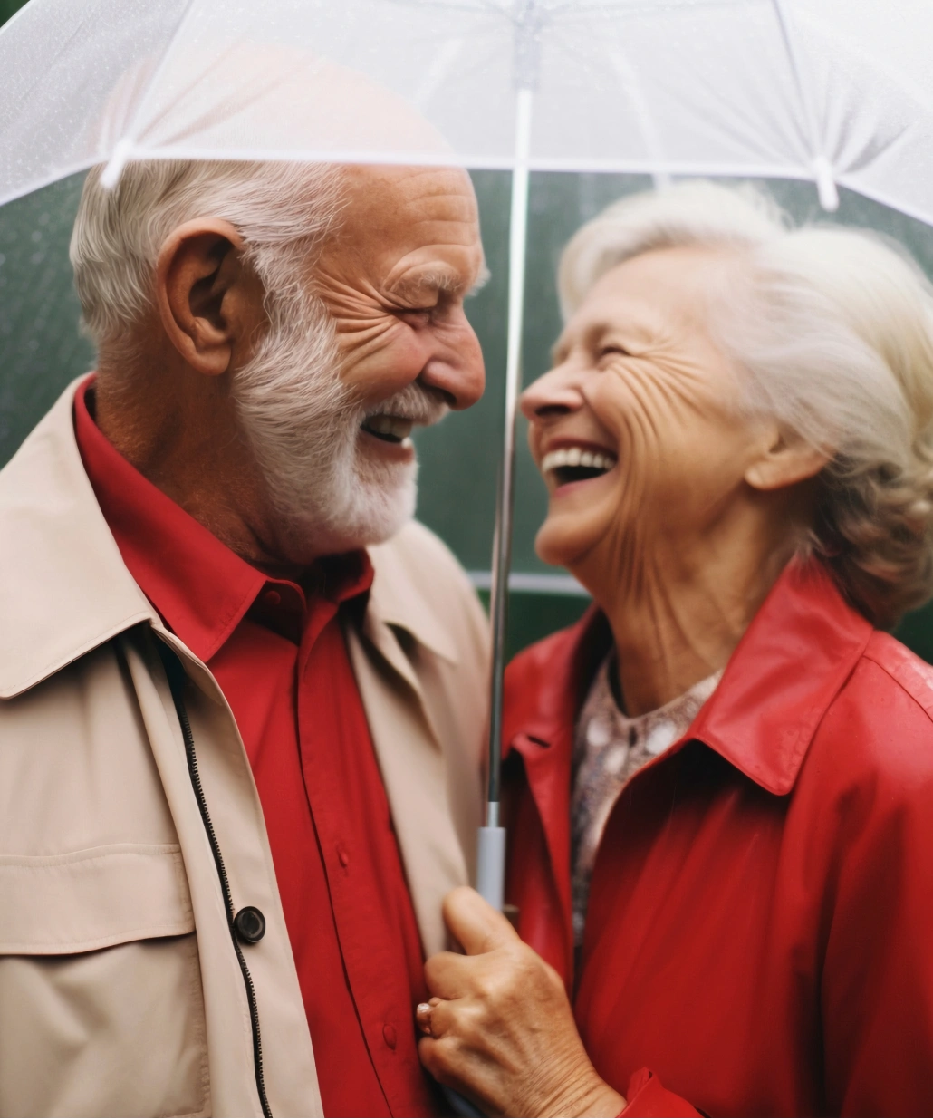 Elderly couple smiling and laughing together under a transparent umbrella on a rainy day.