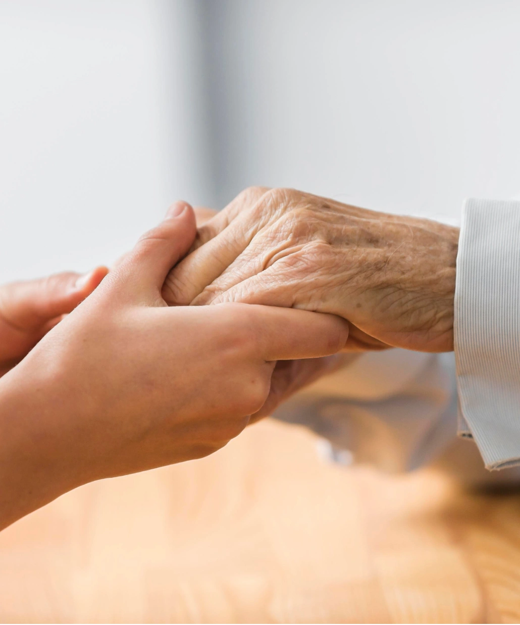 Younger hands gently holding an elderly hand over a wooden surface.