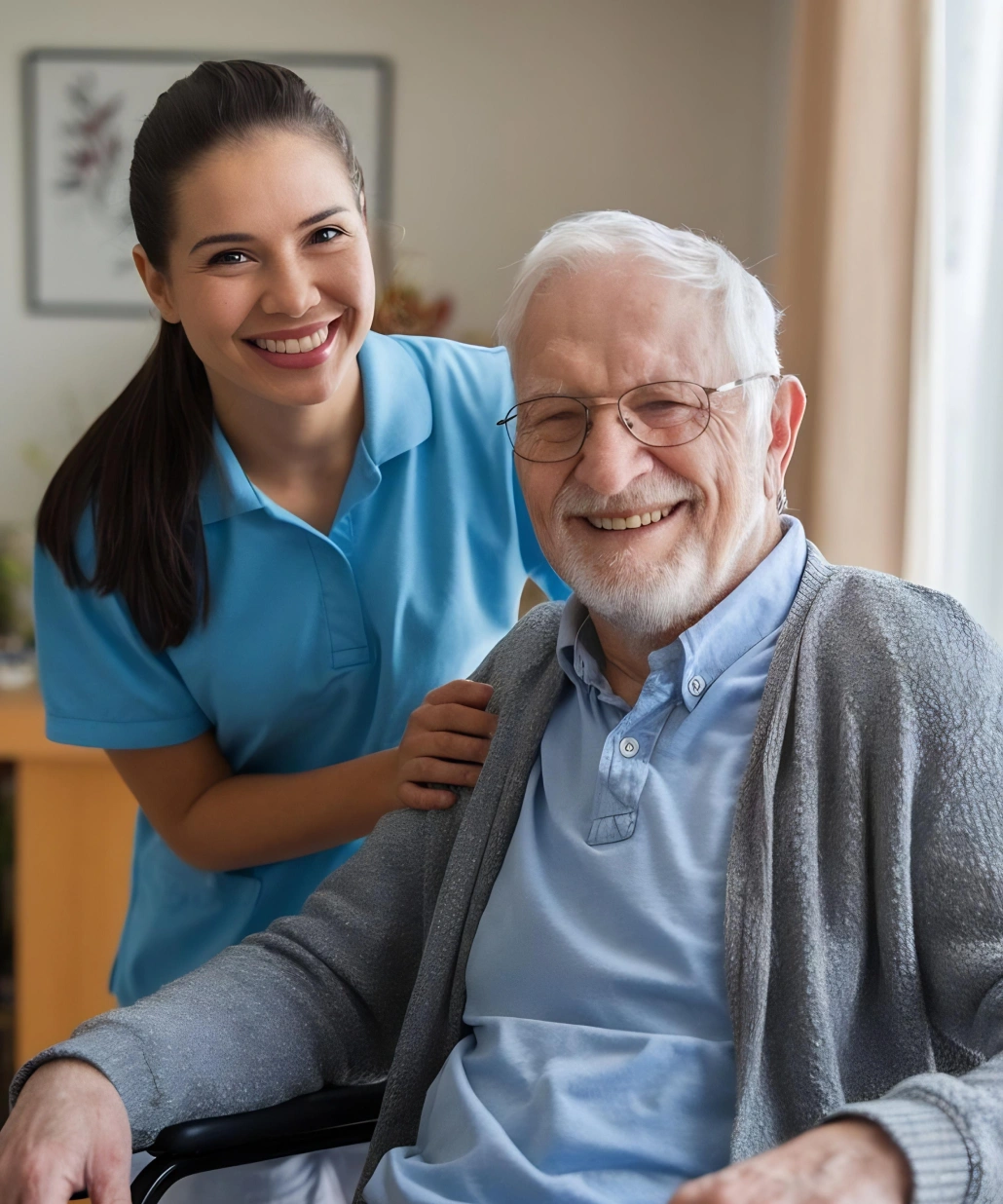 Smiling elderly man in a wheelchair with caring female nurse in blue uniform standing behind him.