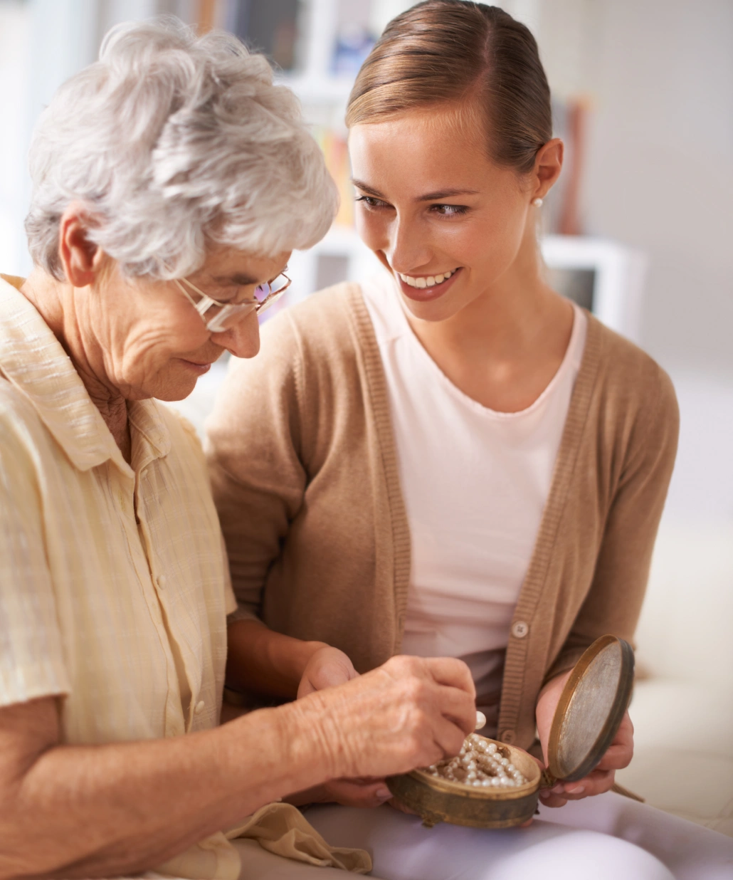 Smiling young woman and elderly woman looking at a pearl necklace in a small open jewelry box.