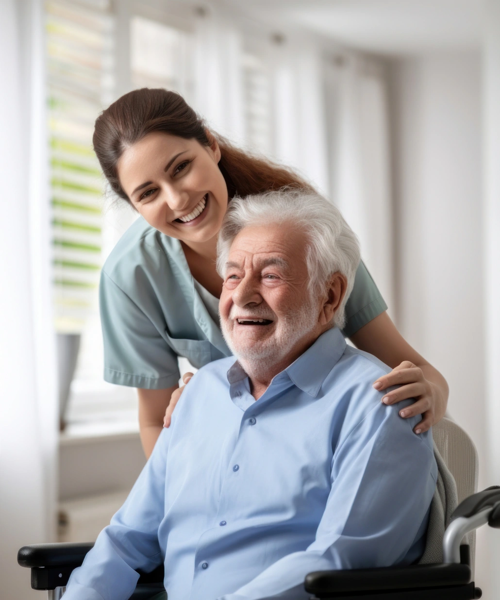 Smiling female caregiver standing behind a happy elderly man in a wheelchair in a bright room.