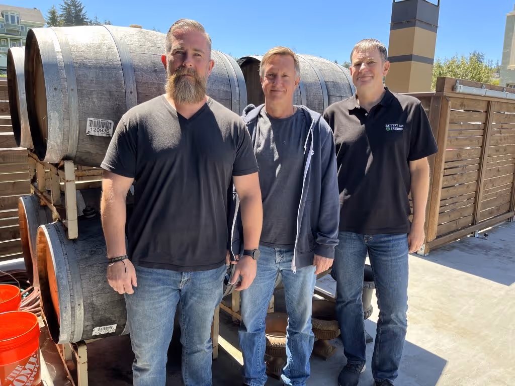 The three owners posing in front of several barrels. from left to right John, Mike, and Jeff