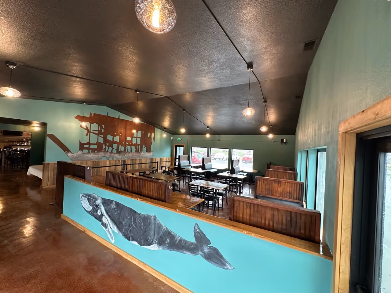 Interior of a restaurant with teal walls, wood booths, tables, and whale murals.