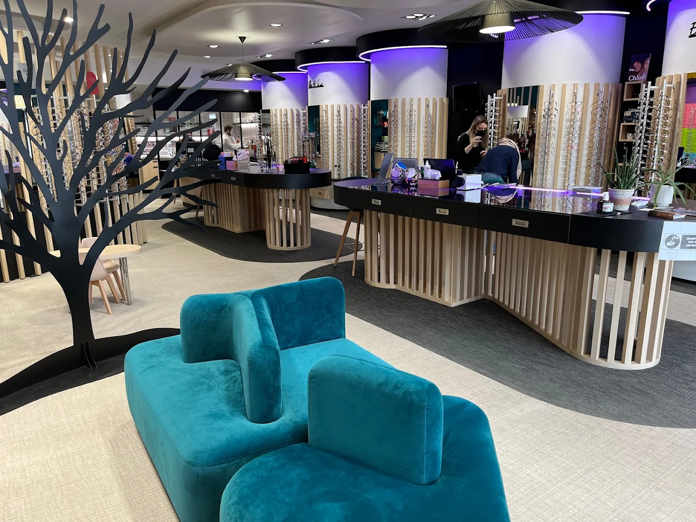 Intérieur d'une boutique d'optique avec présentoirs de montures et canapé bleu