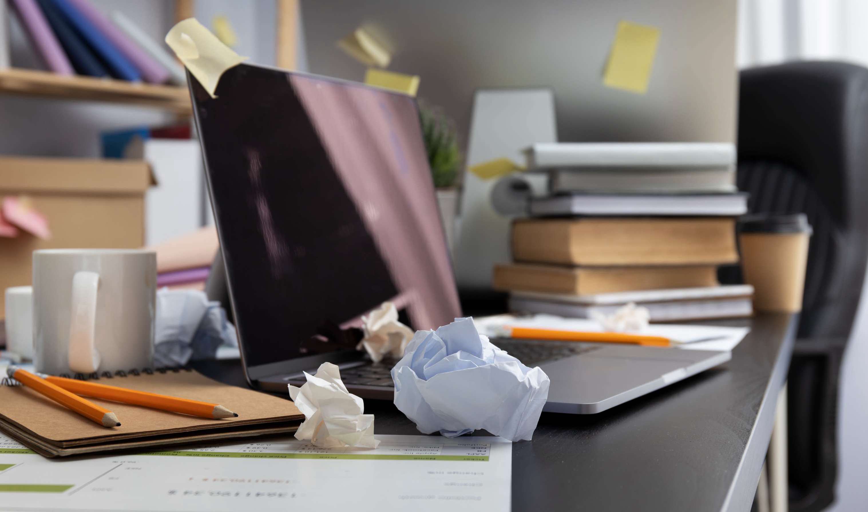 still life image of office desk that is very messy with paper and sticky notes