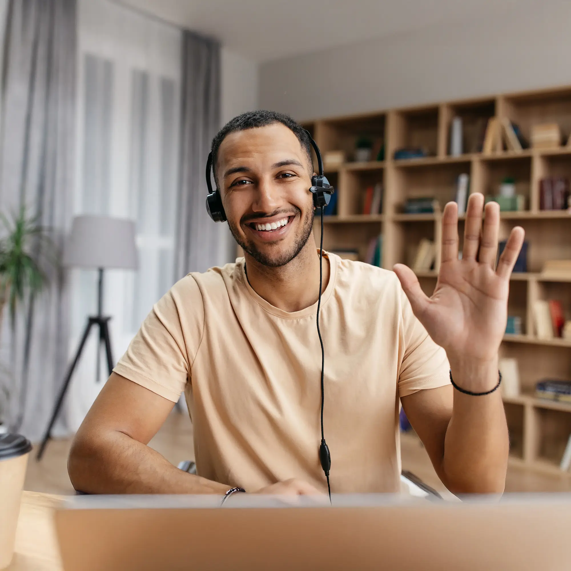 Cheerful man waving during a video interview from a cozy, book-filled home office.