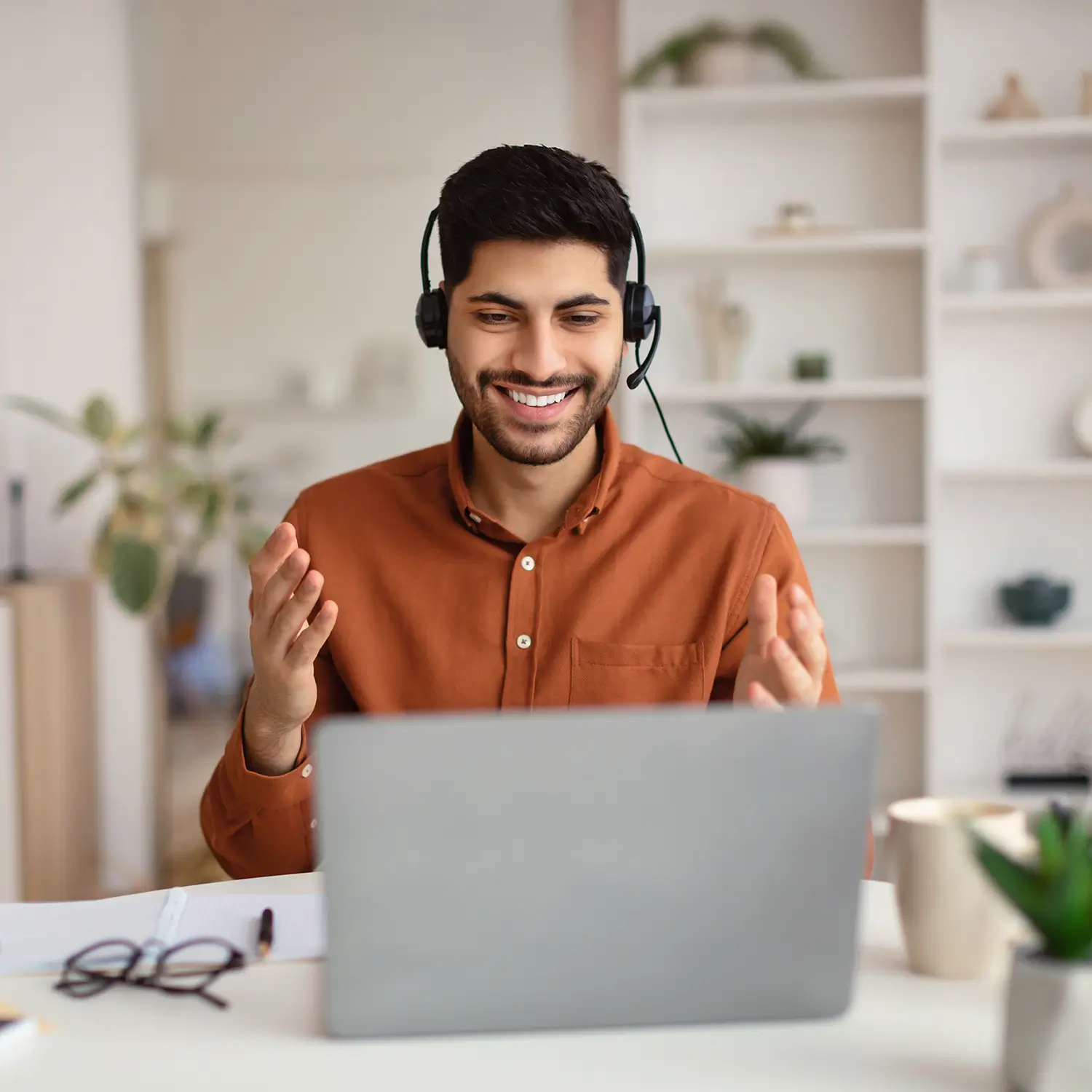 Smiling man in a headset having a virtual meeting on his laptop in a bright home office.
