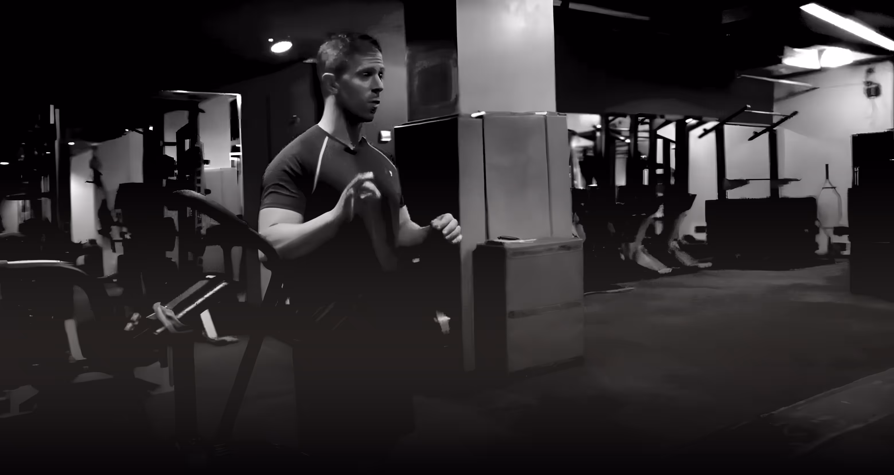 Coach Kev lifting weights in a dimly lit gym.