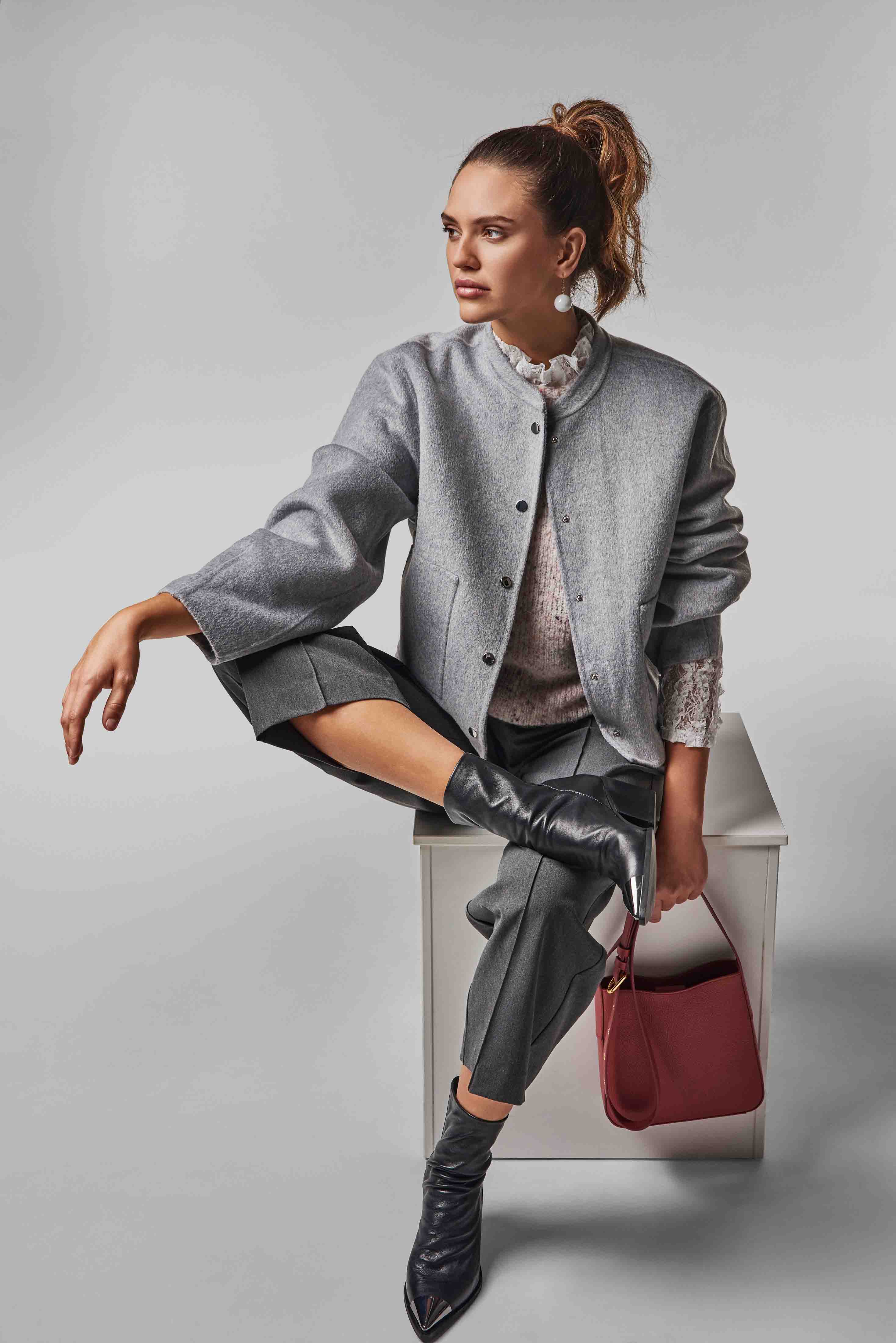 Eine Frau in grauem Outfit sitzt auf einem Block und hält eine rote Tasche in der Hand