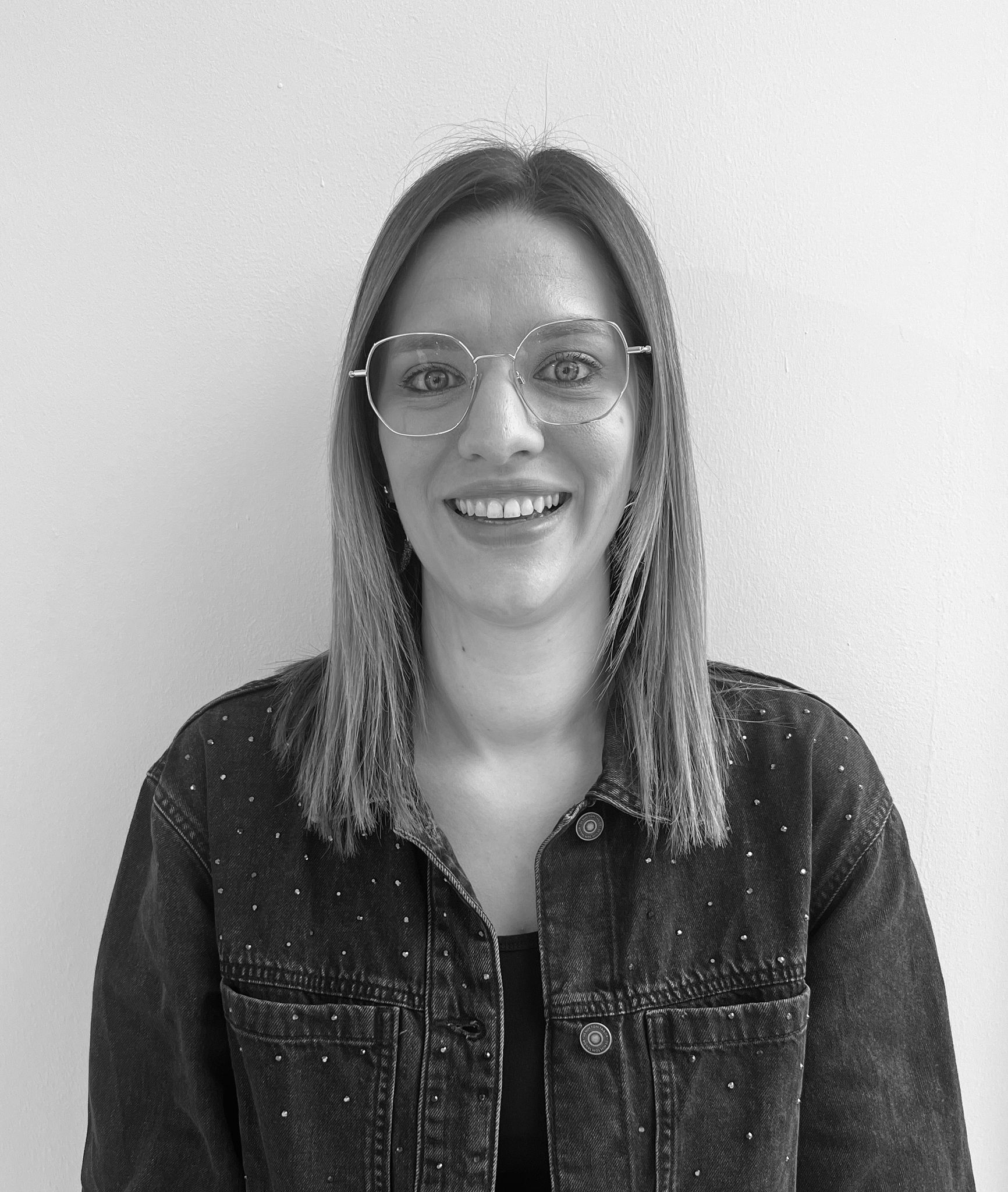 Porträt einer lächelnden Frau mit mittellangen Haaren und Brille, die eine Jacke mit kleinen Nieten trägt.