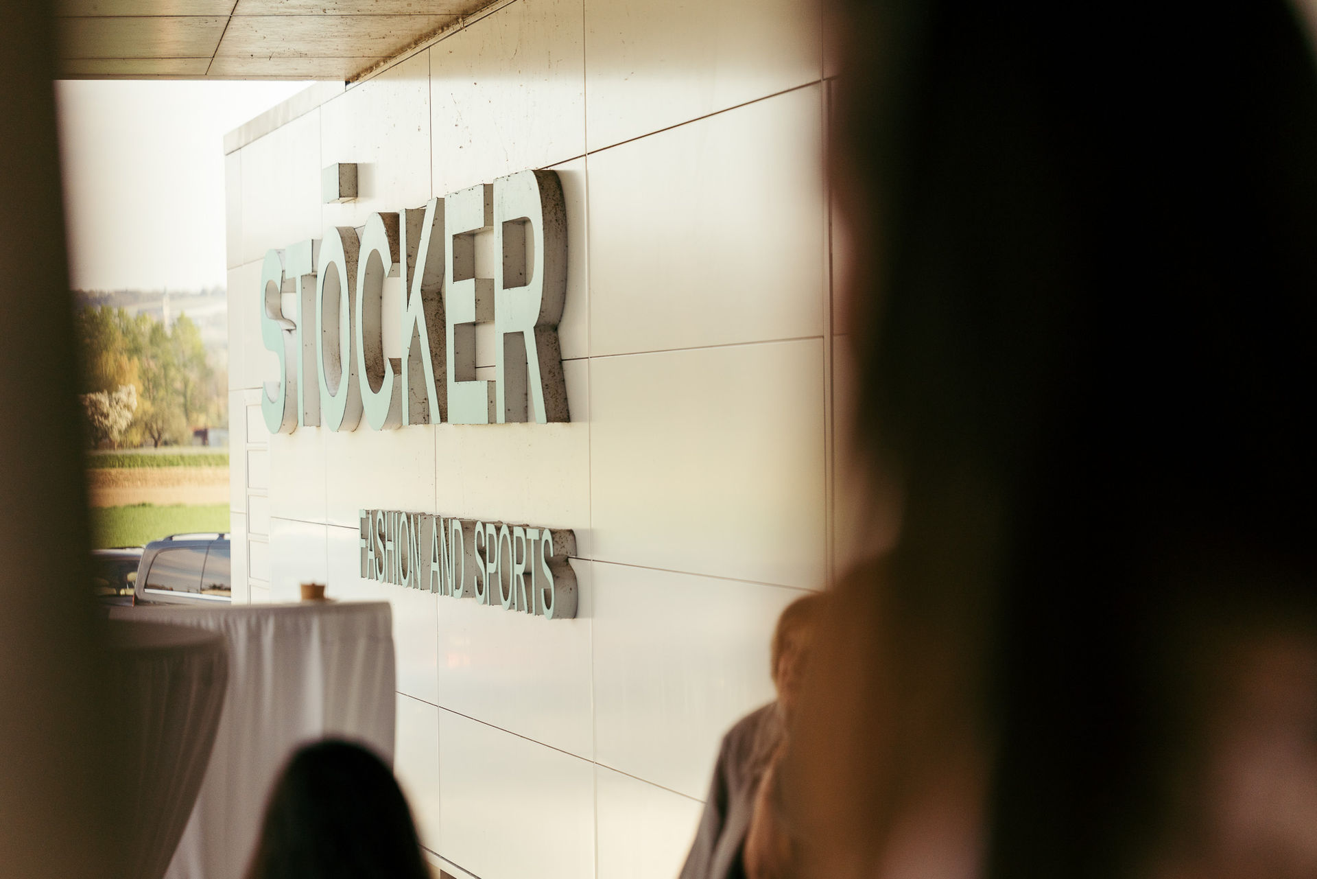 Außenwand mit dem Schriftzug »STÖCKER FASHION AND SPORTS« und unscharfen Personen im Vordergrund.