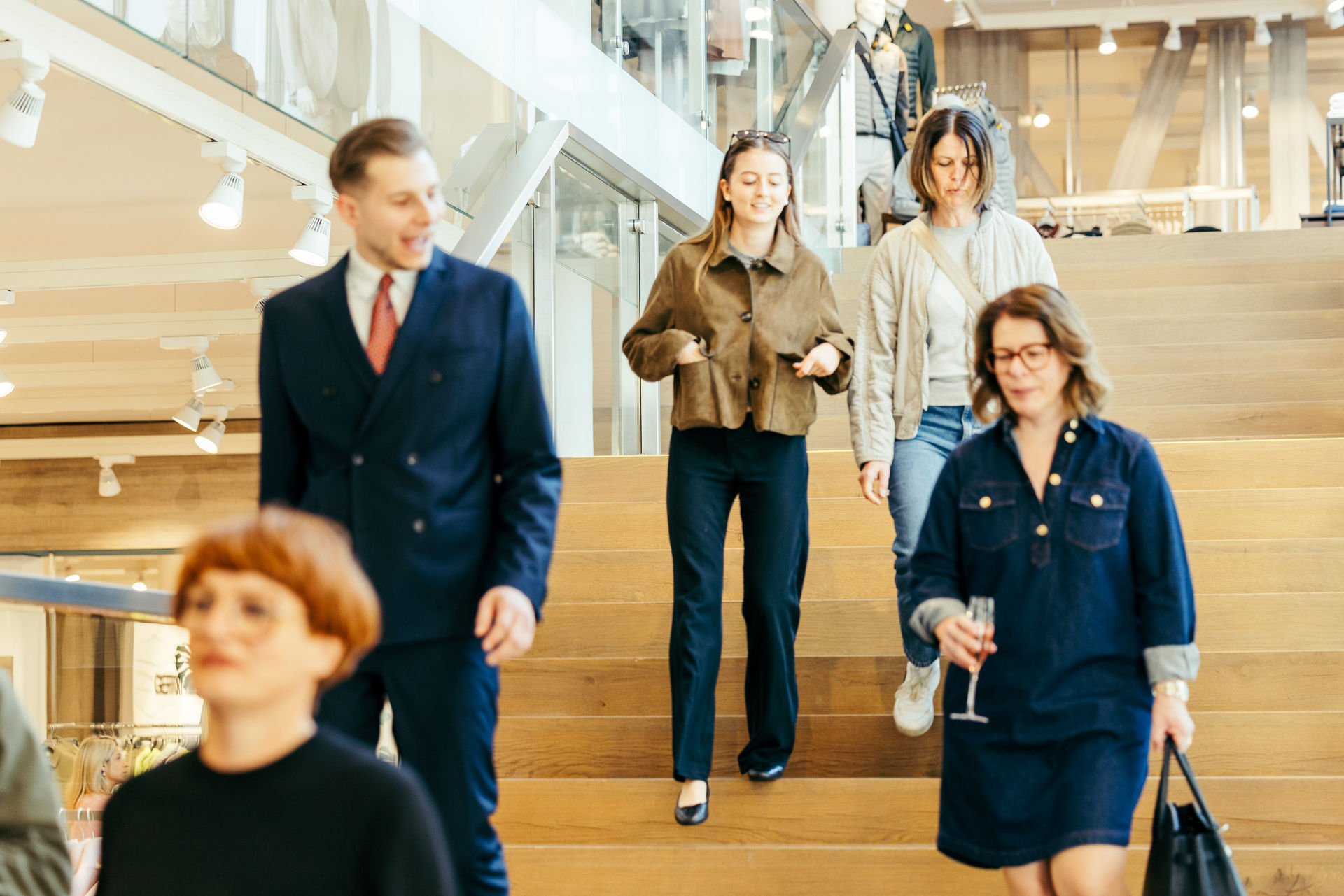 Fünf Menschen, zwei Frauen und ein Mann steigen auf einer großen Holztreppe in einem modernen Geschäft oder Einkaufszentrum ab.