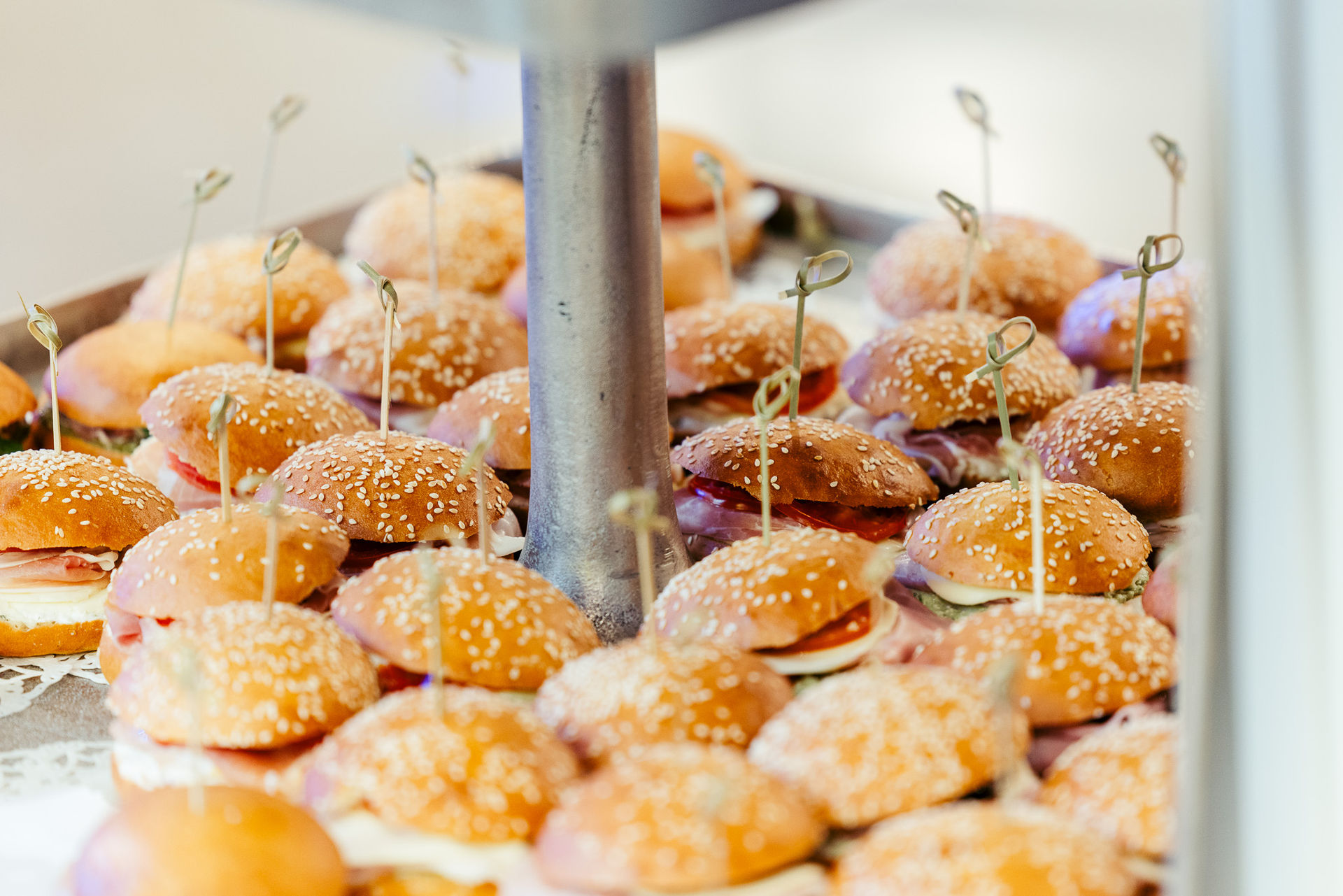 Mehrere kleine Sesambrötchen-Sandwiches mit Schinken und Käse, auf einem Tablett präsentiert.