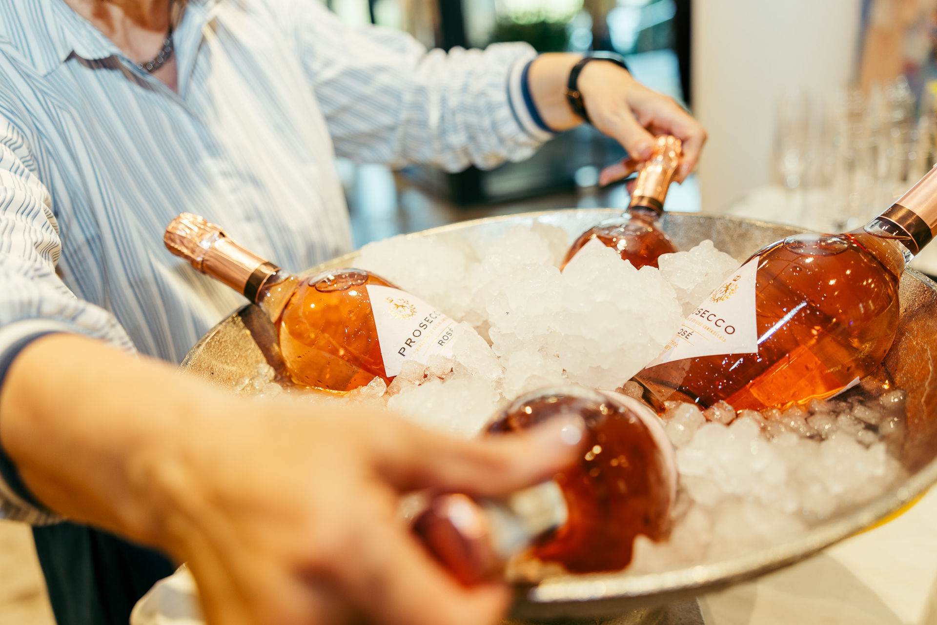 Person hält eine große Schale mit Eis und mehreren Flaschen roséfarbener Prosecco.