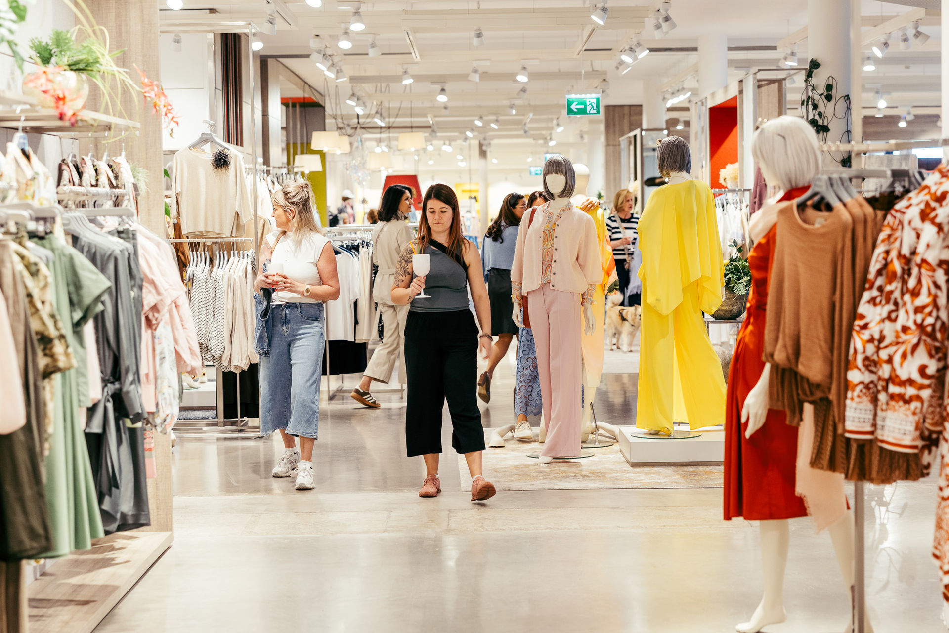 Frauen sehen Kleidung in einem hell beleuchteten Modegeschäft mit Mannequins und dekorierten Kleiderständern.