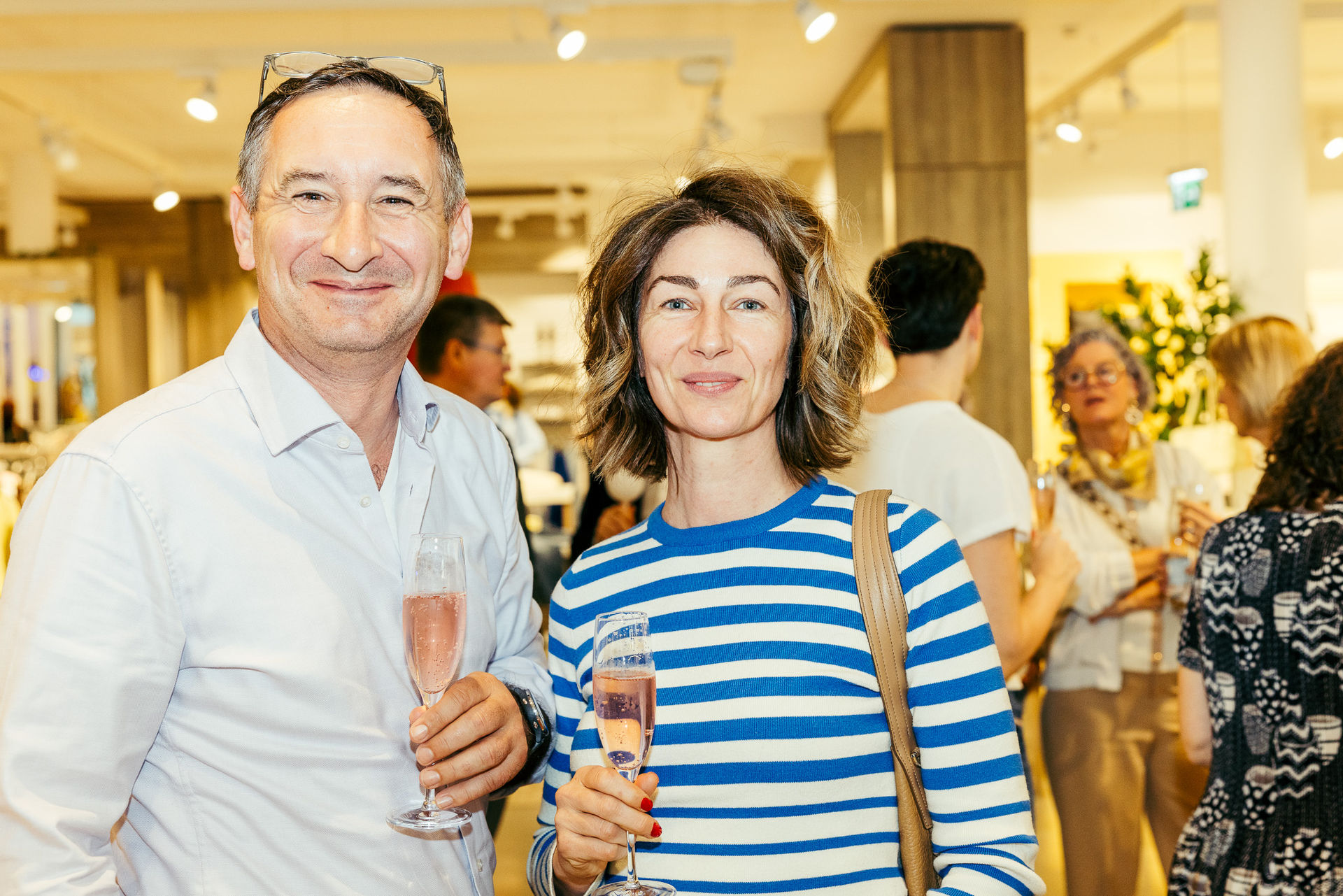 Ein Mann und eine Frau lächeln, während sie in einem gut beleuchteten Raum ein Glas Sekt halten.
