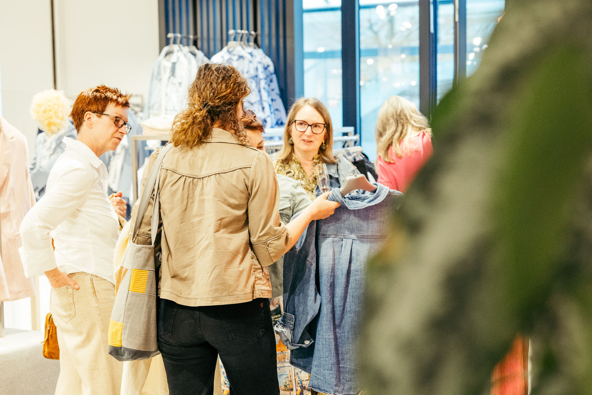 Fünf Frauen in einem Bekleidungsgeschäft, eine hält eine blaue Jeansjacke an einem Kleiderbügel hoch und zeigt sie den anderen.