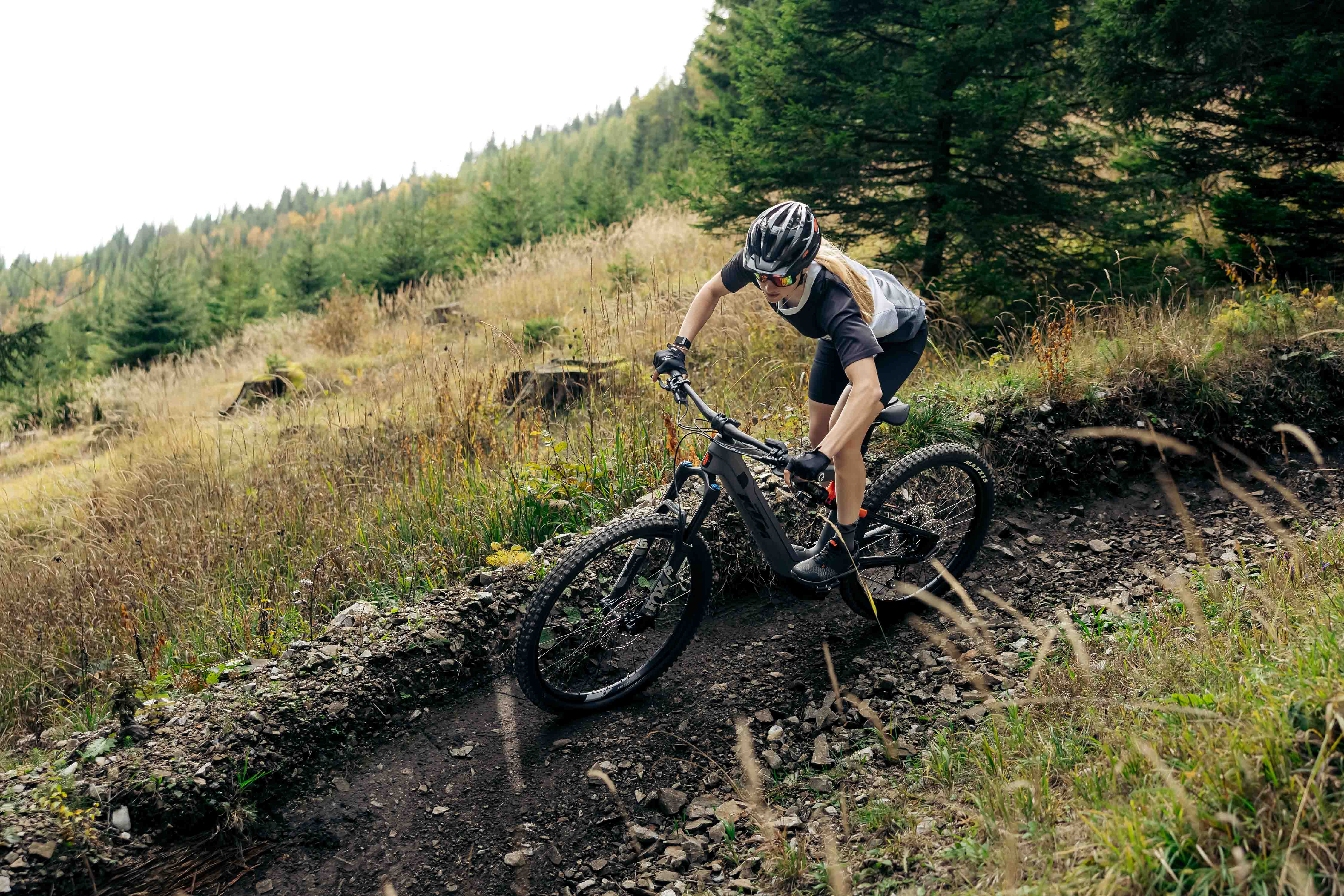 Frau fährt mit Mountainbike auf schmalem Waldweg mit steilen Kurven und grünen Bäumen.