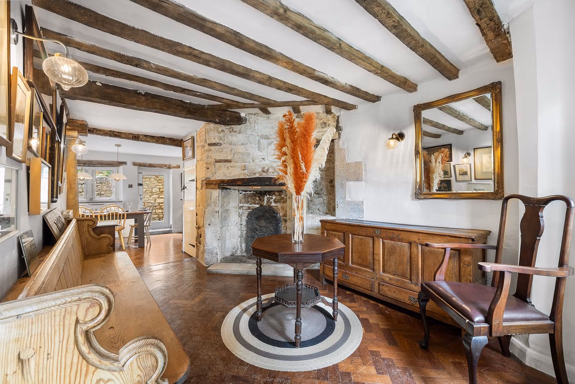 Rustic cottage interior with stone fireplace, wooden beams, and pampas grass