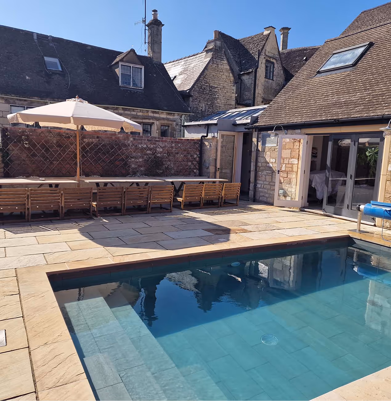 Stone house with swimming pool and wooden seating area under sun umbrella