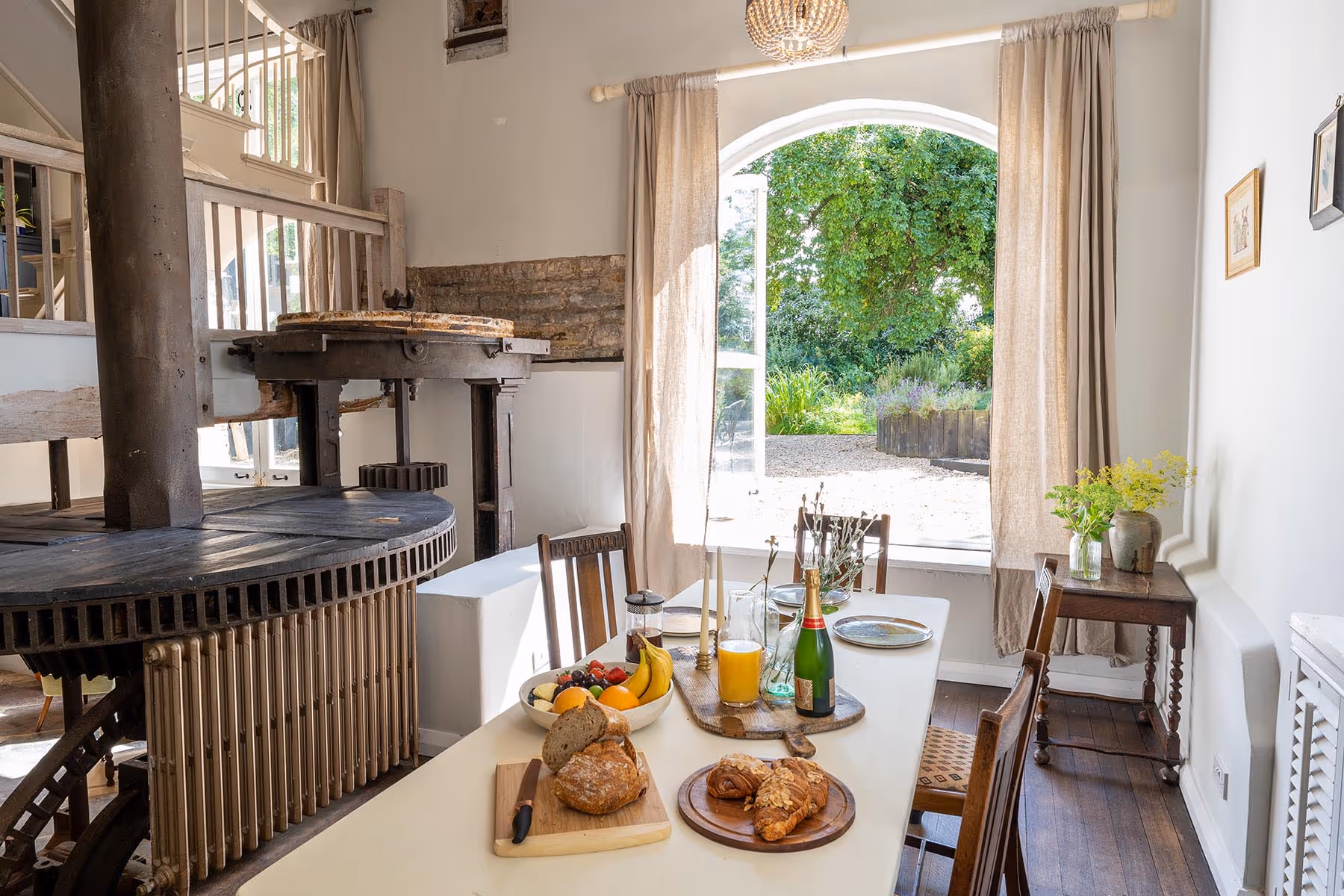 Rustic dining area with breakfast spread, vintage mill machinery, and garden view