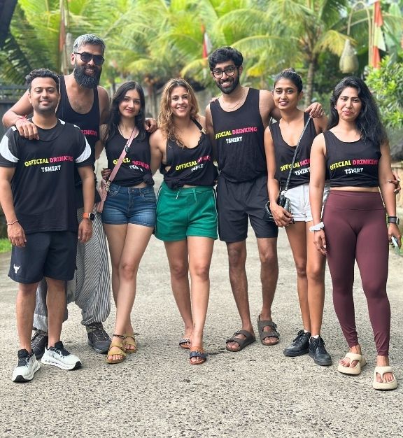 Smiling man with dark hair and beard wearing a dark gray t-shirt, standing with arms crossed.