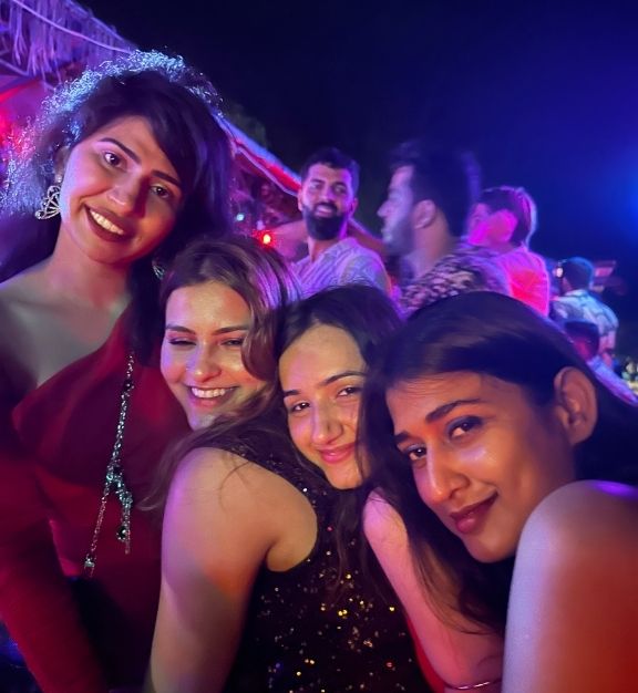 Group of four young women smiling and posing closely together at a nighttime party with colorful lights with Triptease