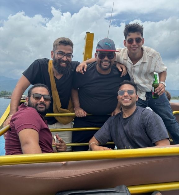 Group of five men smiling and posing on a boat with cloudy sky and mountains in the background in bali with triptease