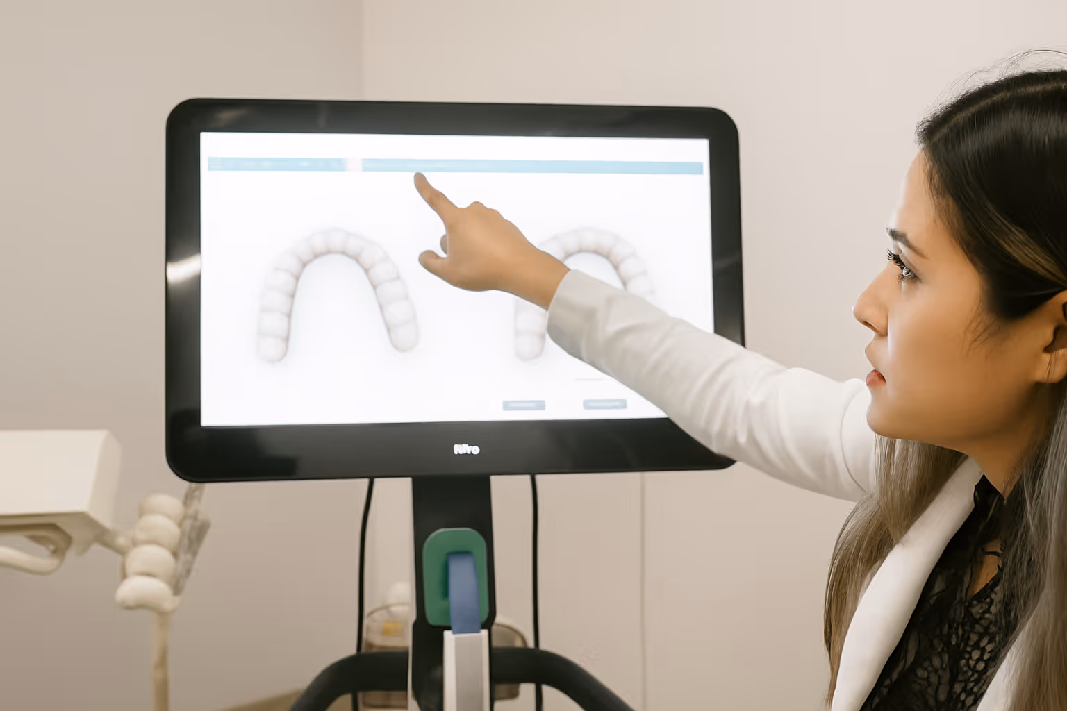 Dr. Rupporn Priyawat in a white lab coat pointing at dental arch images displayed on a screen Smiling woman holding an Invisalign kit box with the text 'Your smile is just the beginning' inside the lid at Omnia Dental Care in Chino Hills, CA