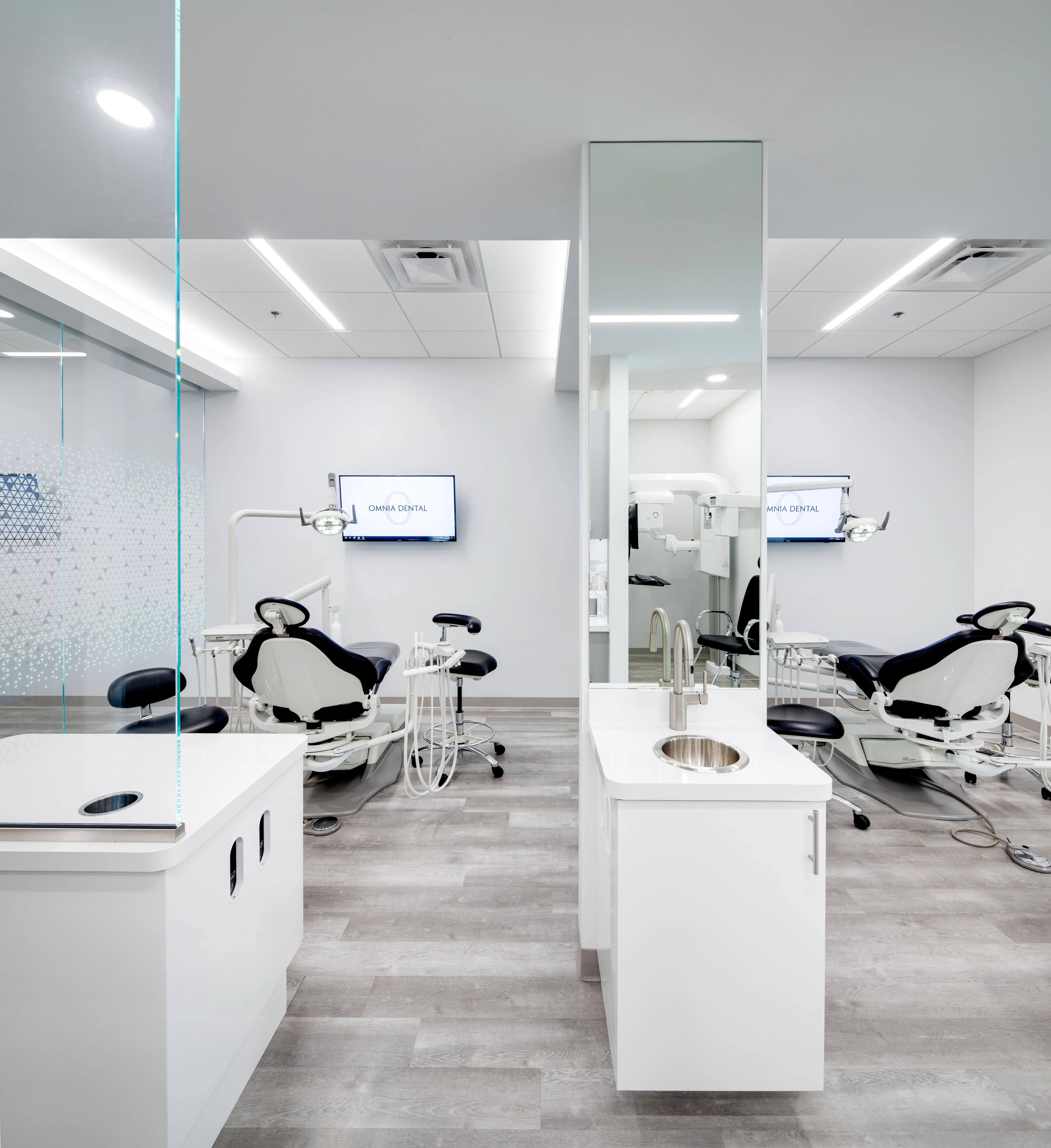 Modern dental clinic room with two dental chairs, a large mirror with a sink, and screens displaying 'OMNIA DENTAL.' at Omnia Dental Care in Chino Hills, CA 