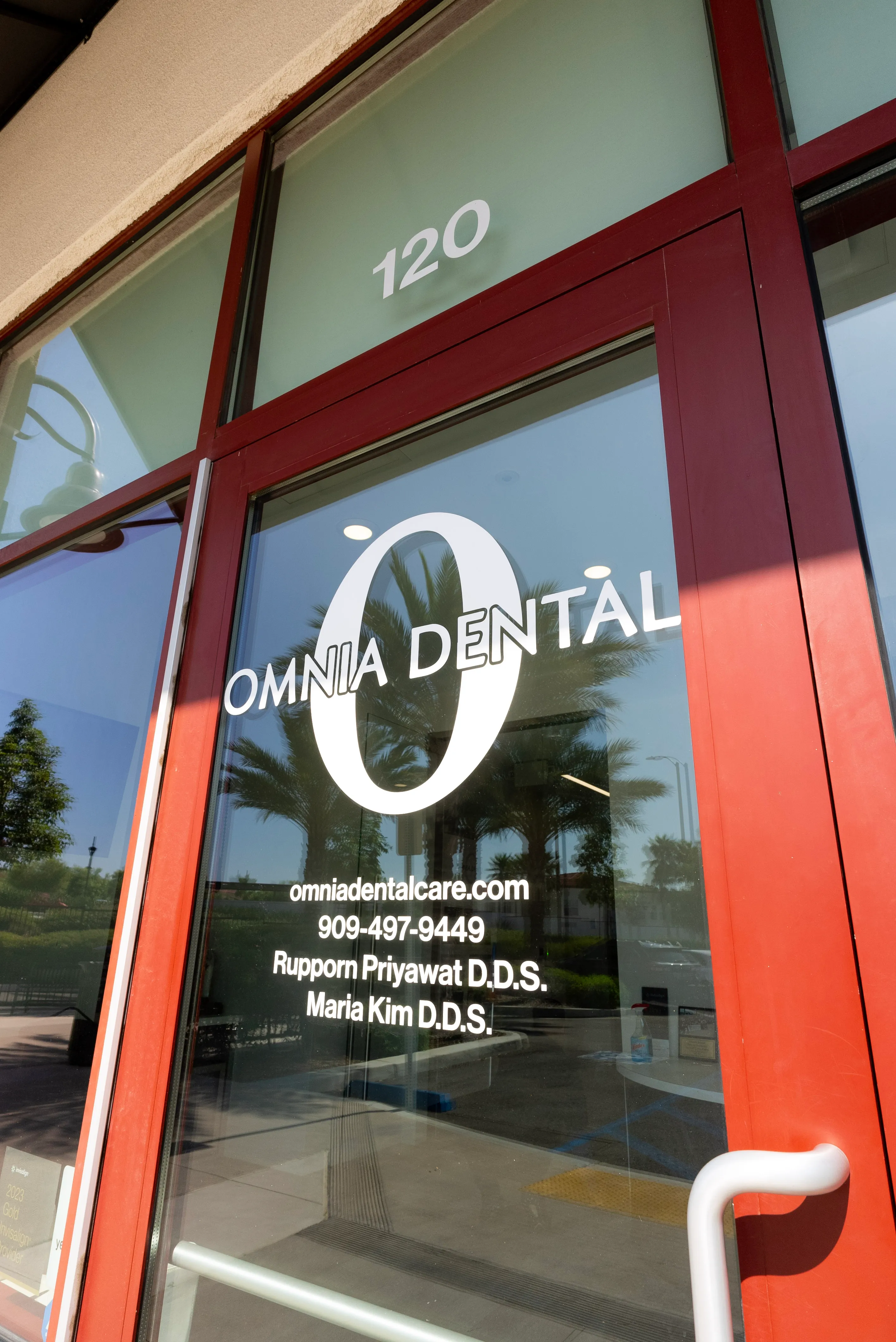 Glass door of Omnia Dental office with contact details and names of dentists Rupporn Priyawat D.D.S. and Maria Kim D.D.S.