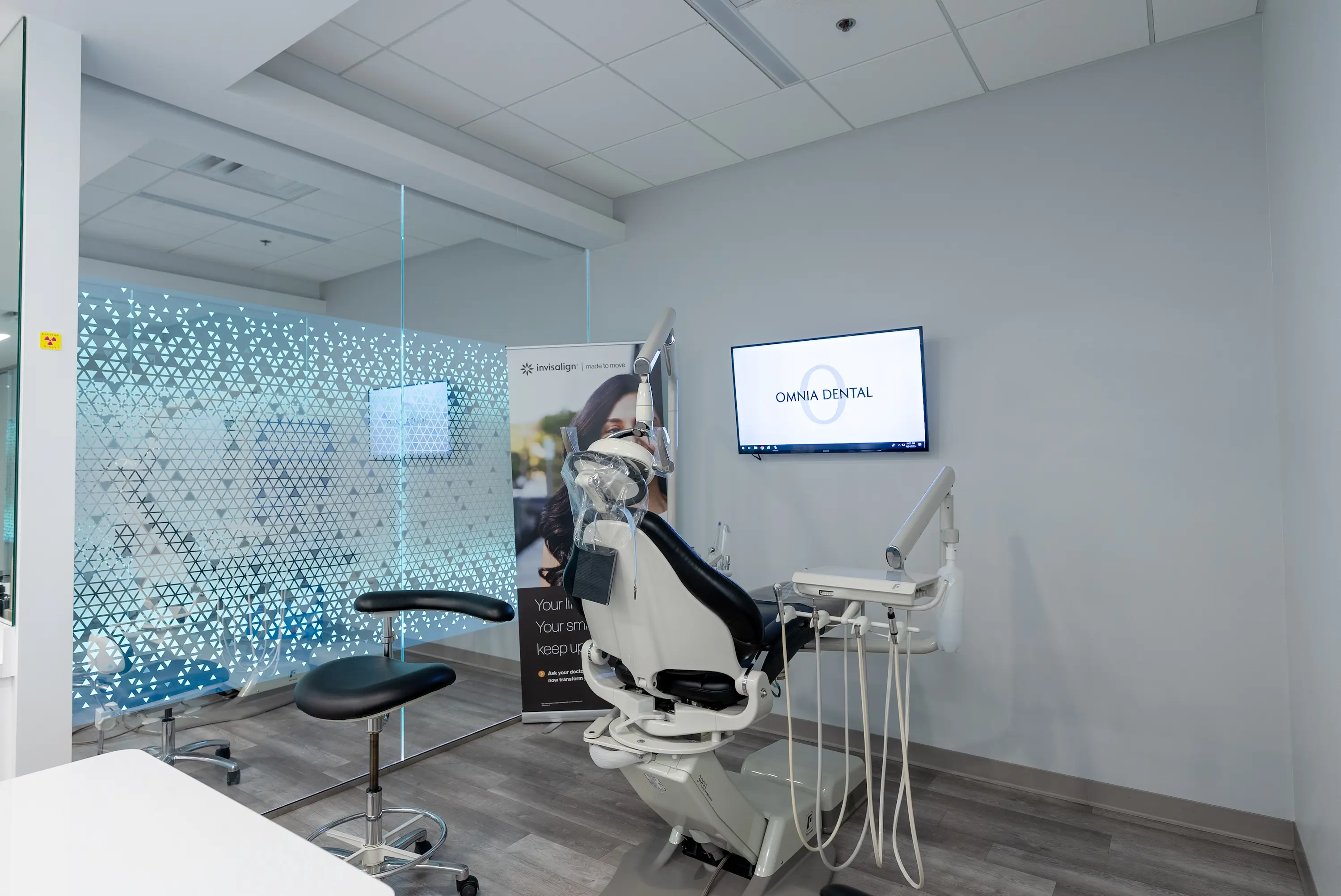 Modern dental examination room with a white dental chair, dental tools, and a wall-mounted screen displaying Omnia Dental logo at Omnia Dental Care in Chino Hills, CA 