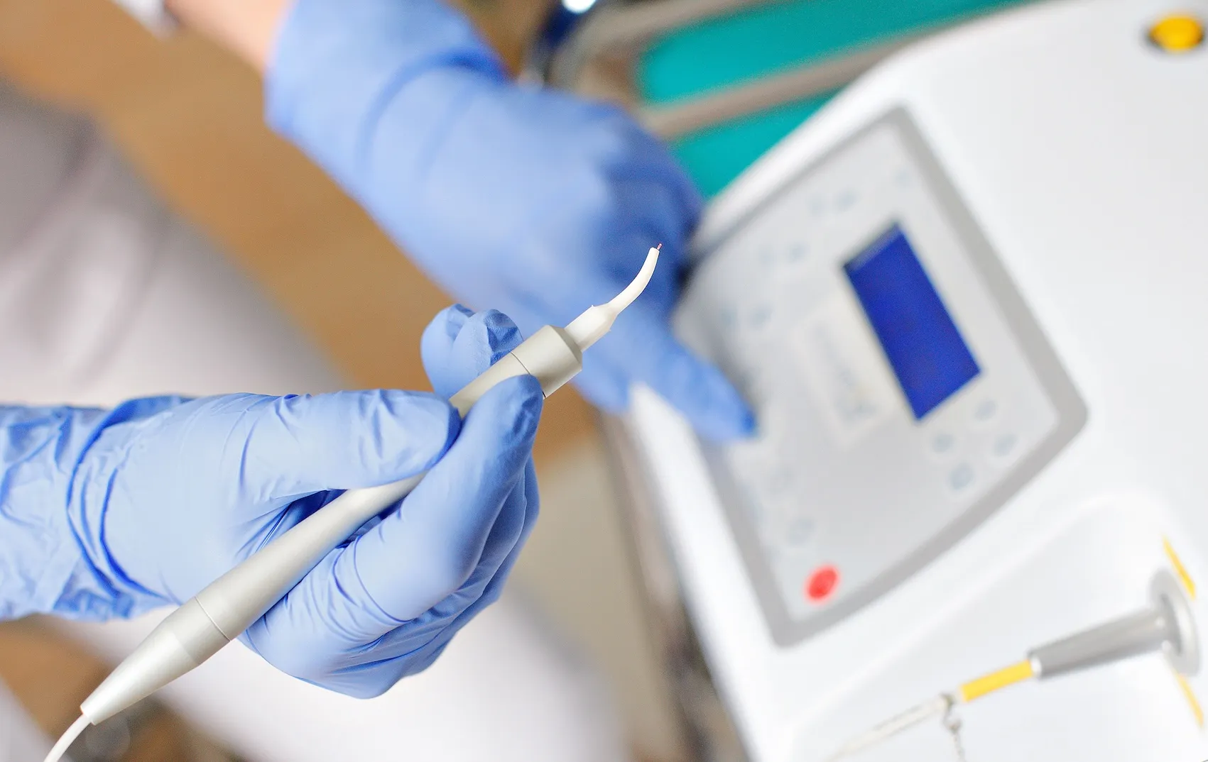 Gloved hands holding a dental diode laser handpiece beside the control unit at Omnia Modern Dentistry in Chino Hills CA