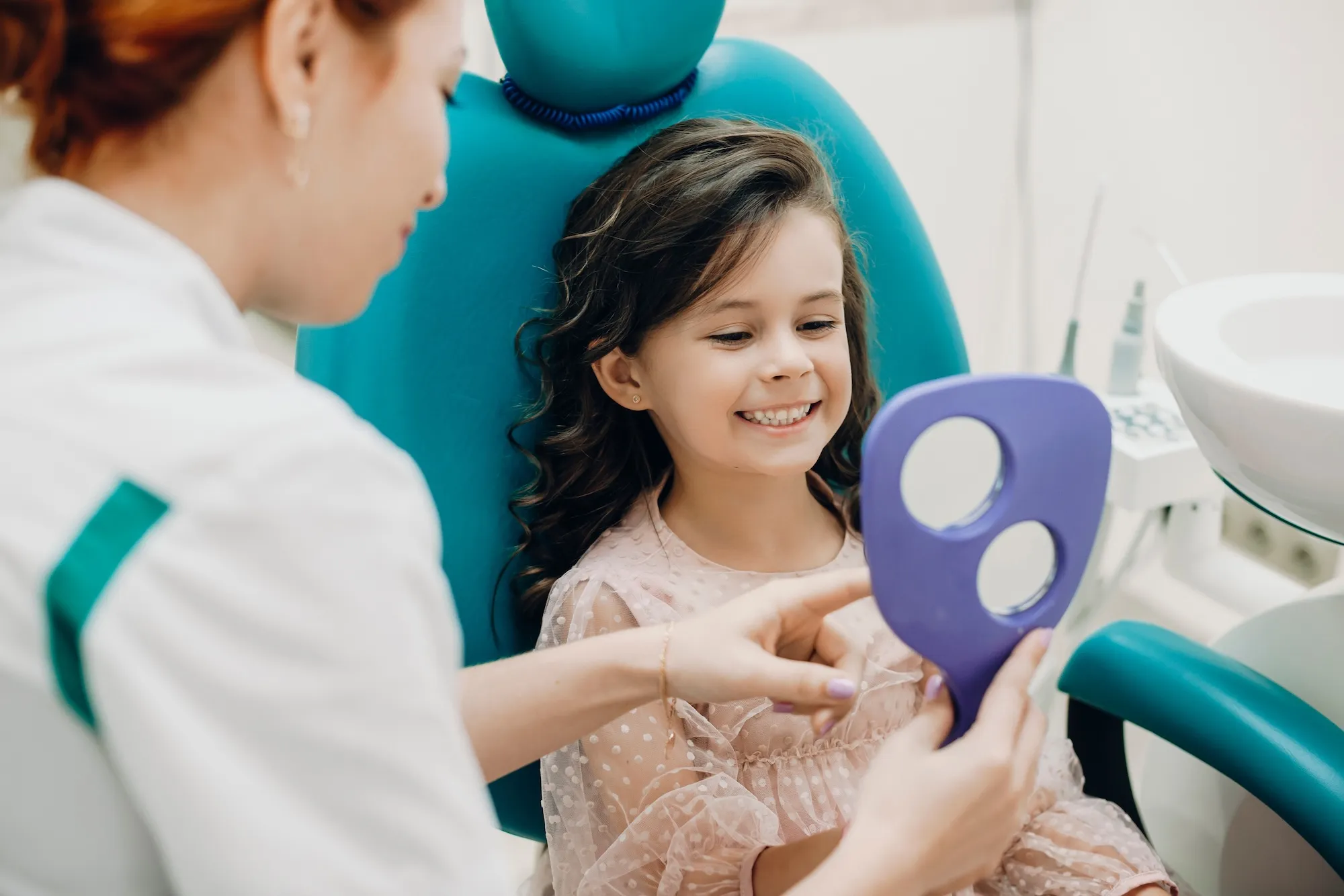 Smiling young girl in the dental chair looking at her teeth in a hand mirror with her dentist at Omnia Modern Dentistry in Chino Hills, CA