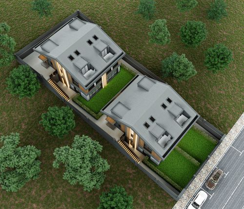 Modern semi-detached houses with large A-frame roofs and expansive glass windows, featuring metal balconies and dark tiled roofing, illuminated by warm evening sunlight.