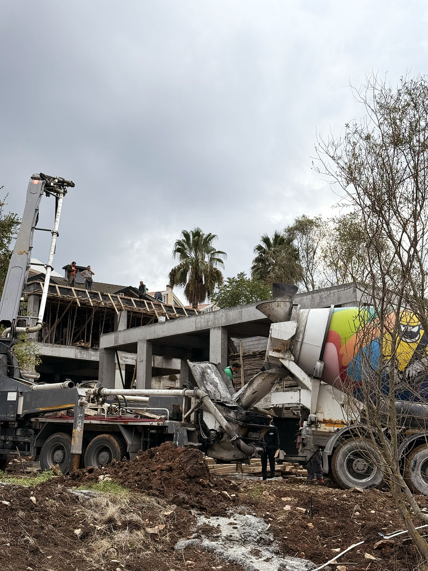 Modern white duplex with flat roofs, solar panels, glass balconies, and geometric design, surrounded by a black gate and shrubs, under clear blue sky in sunny residential neighborhood.