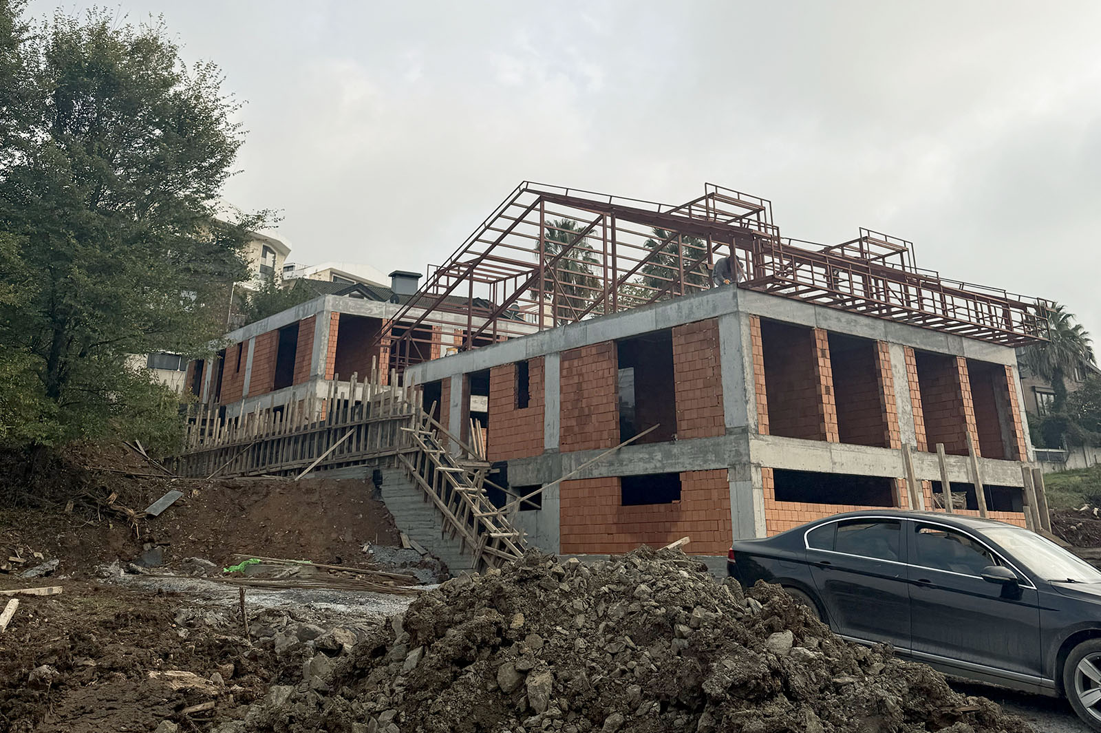 Modern semi-detached houses with large A-frame roofs and expansive glass windows, featuring metal balconies and dark tiled roofing, illuminated by warm evening sunlight.