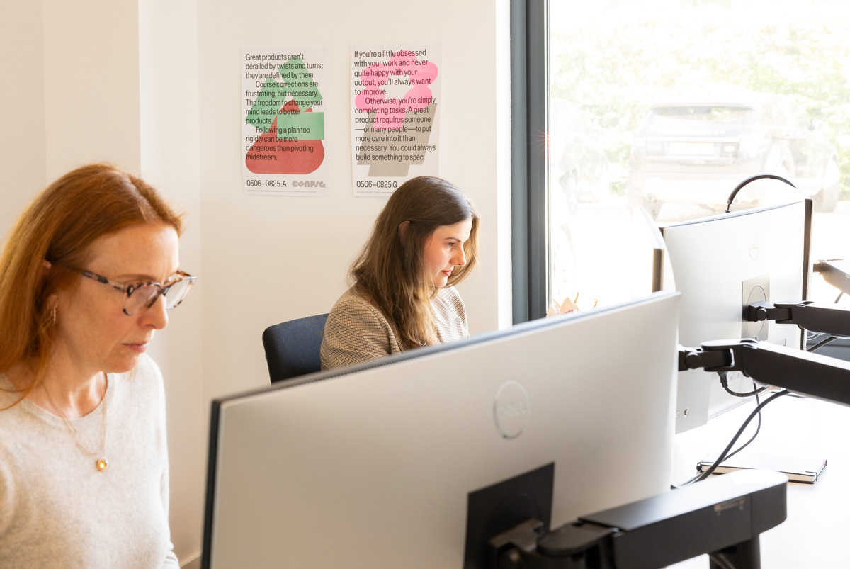 Two women working at desks with large computer monitors in a modern office.
