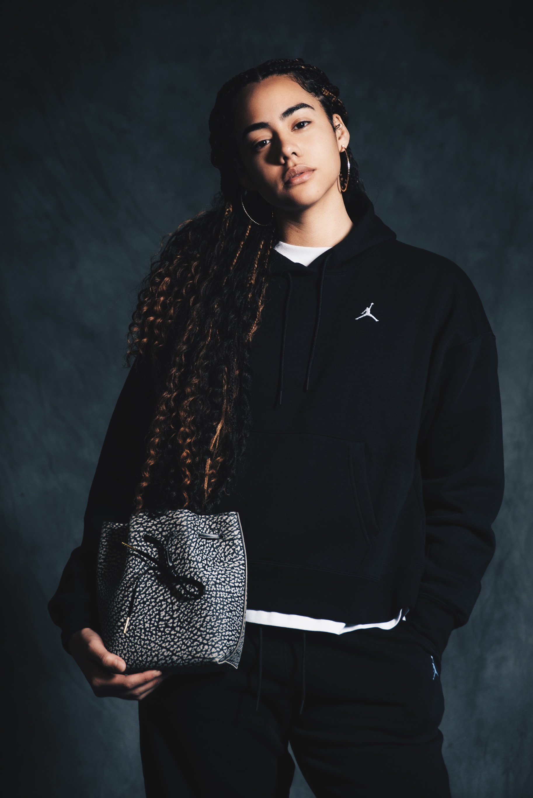A woman in a Jordan sweatsuit holding a SUNDRIES cement bucket bag.