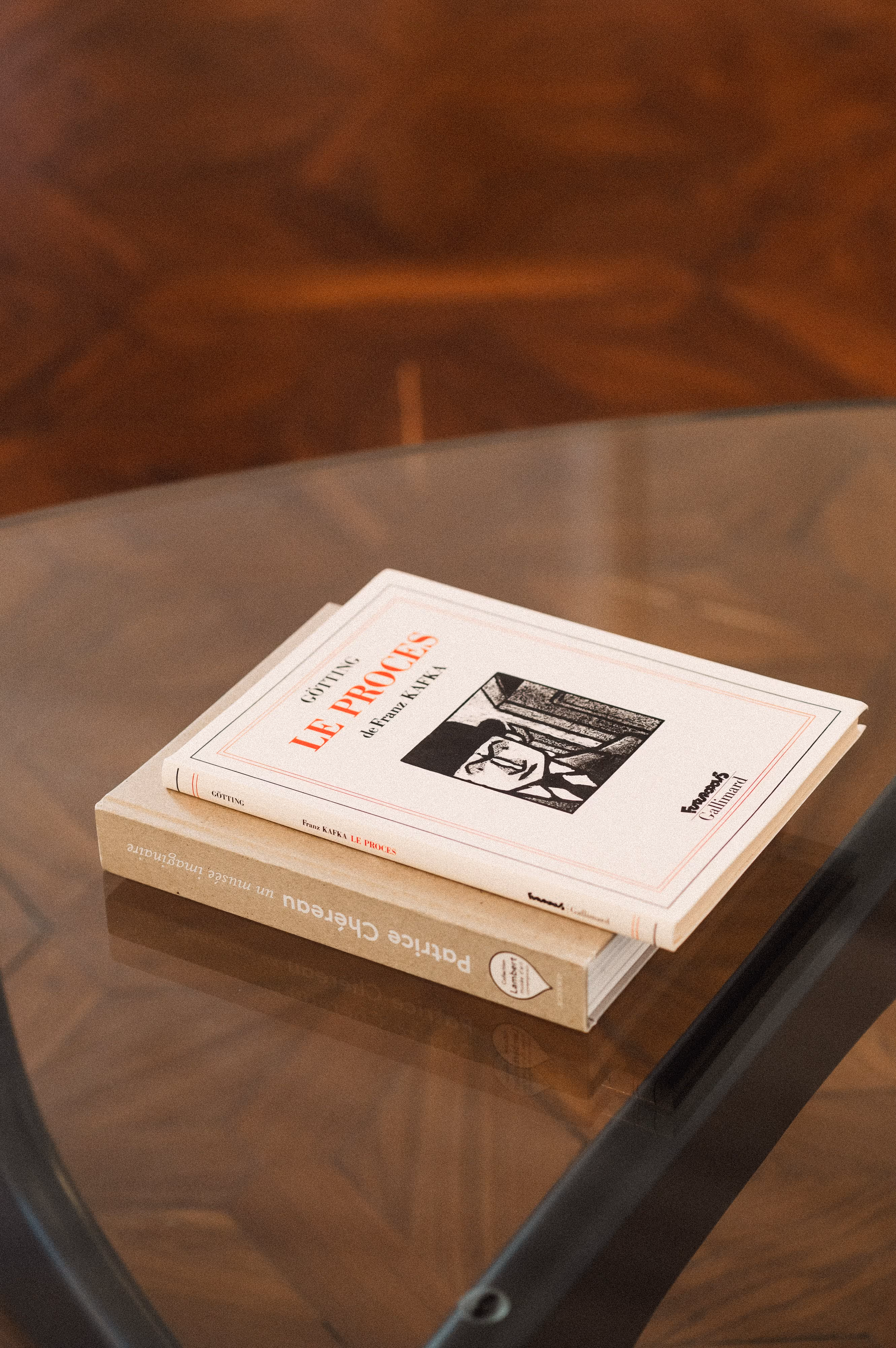 Deux livres empilés sur une table en verre, le livre du dessus est 'Le Procès' de Franz Kafka.