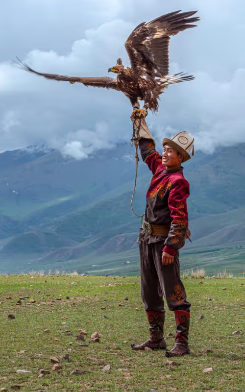 An image showing an Eagle hunter in Kyrgyzstan near Issyk Kul lake who is smiling and showing off his skills to behind the science adventurers. 