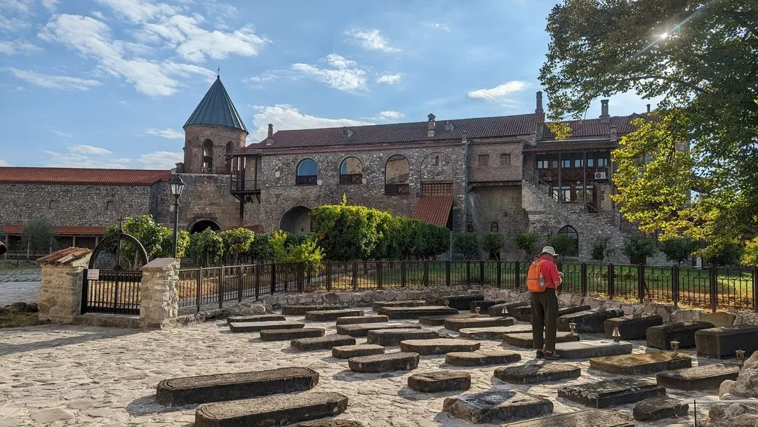 Historic monastery in Georgia with a stone courtyard and ancient graves, surrounded by lush greenery.