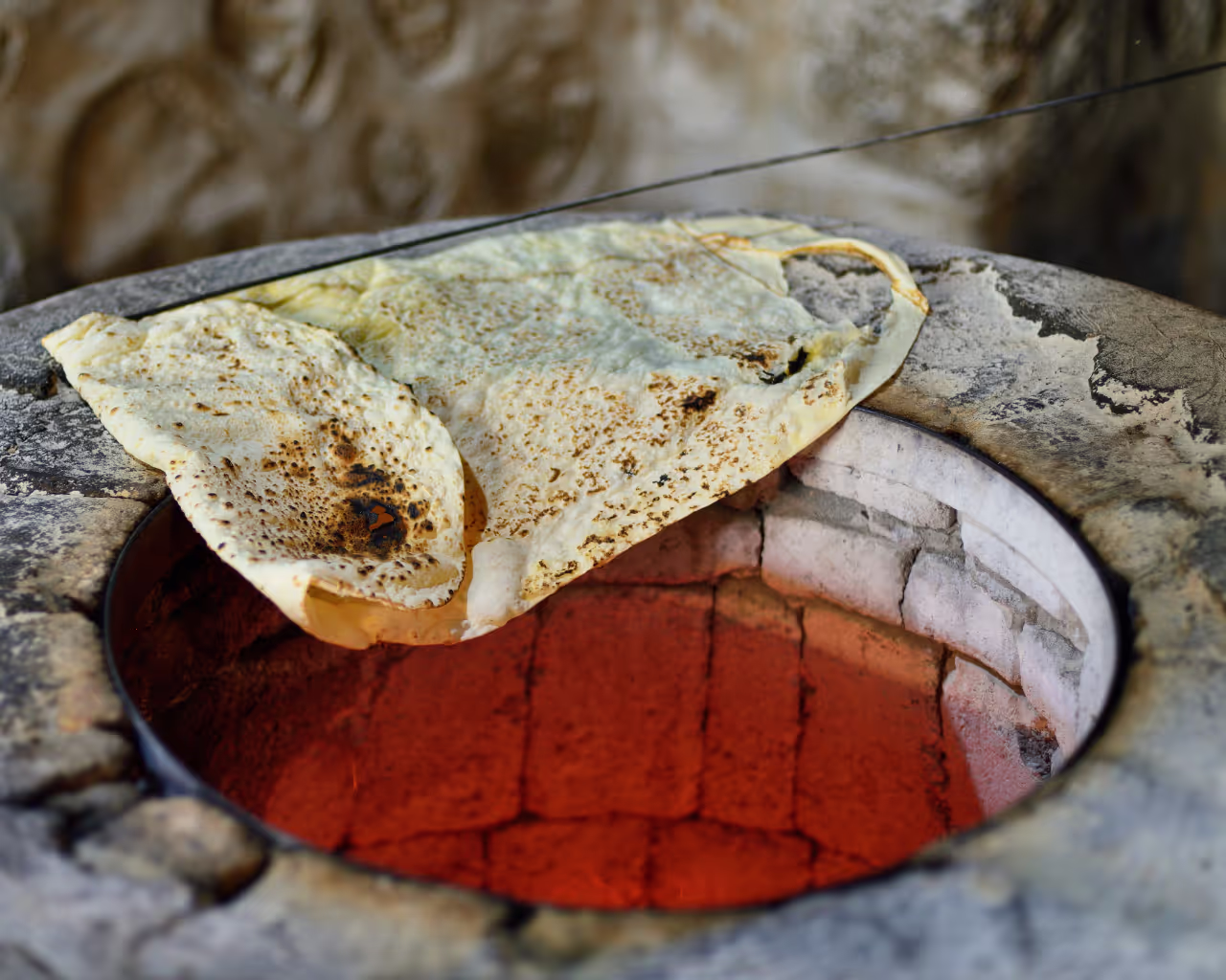 Traditional Armenian lavash bread baking in a hot tonir oven, slightly charred and golden brown.
