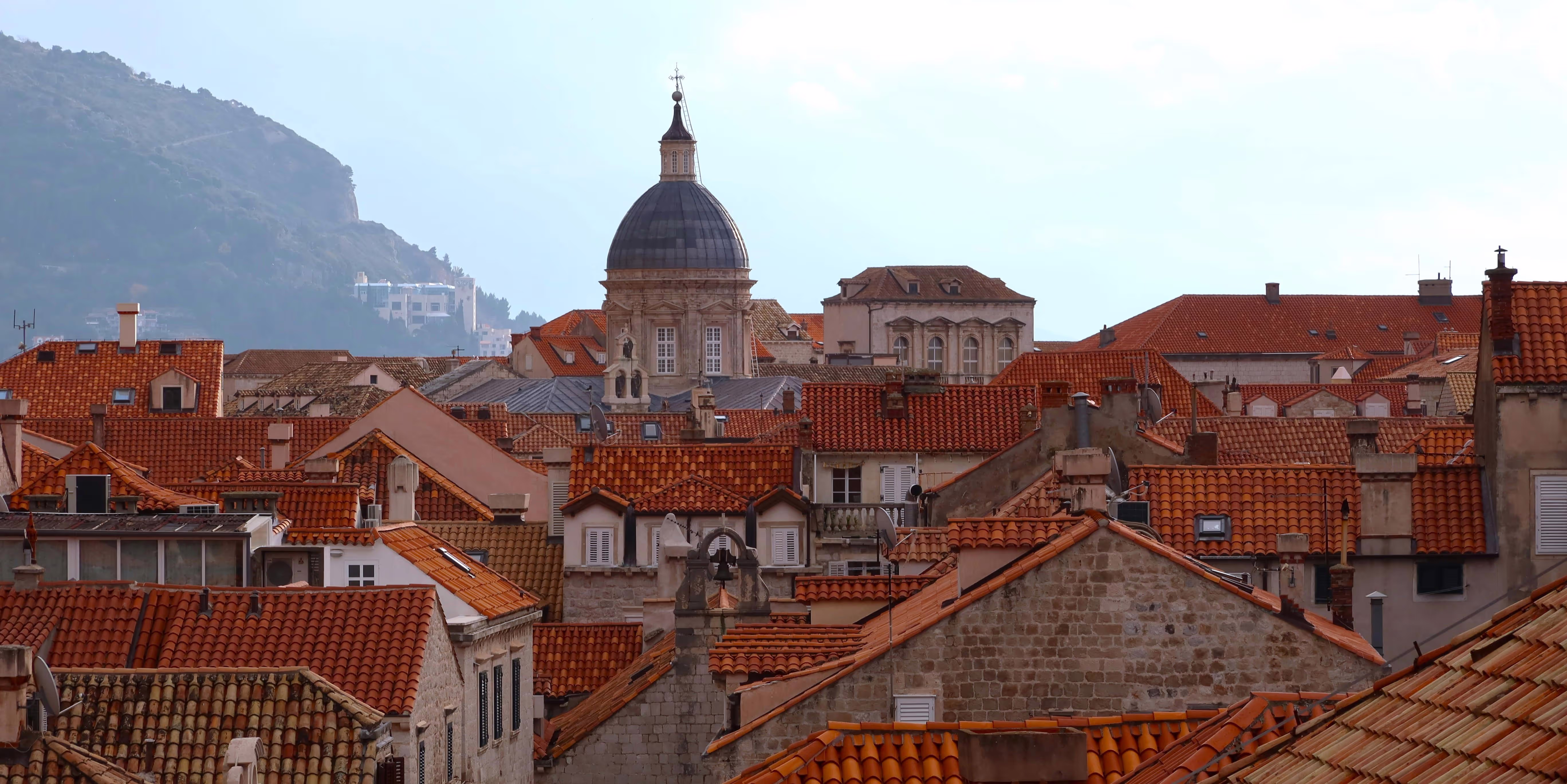 The terracotta rooftops of Dubrovnik Old Town, Croatia, with a large domed cathedral rising above them.