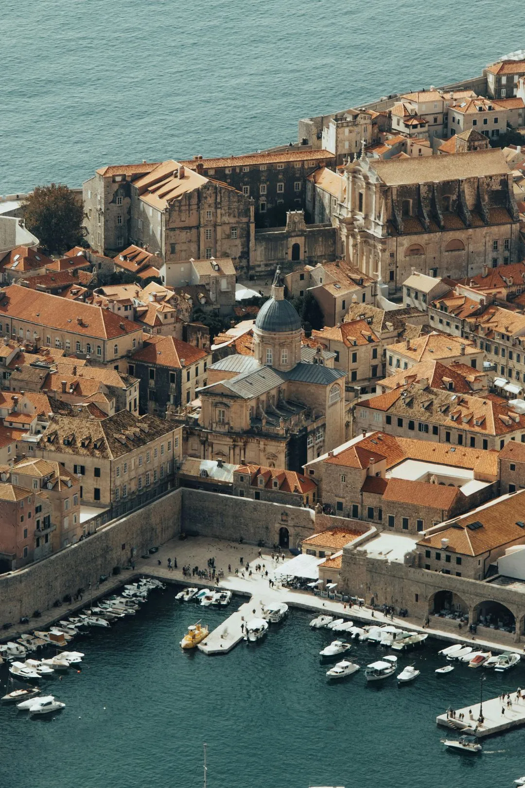 Aerial view of Dubrovnik Old Town, Croatia, showing medieval architecture, a harbor with boats, and the Adriatic Sea.