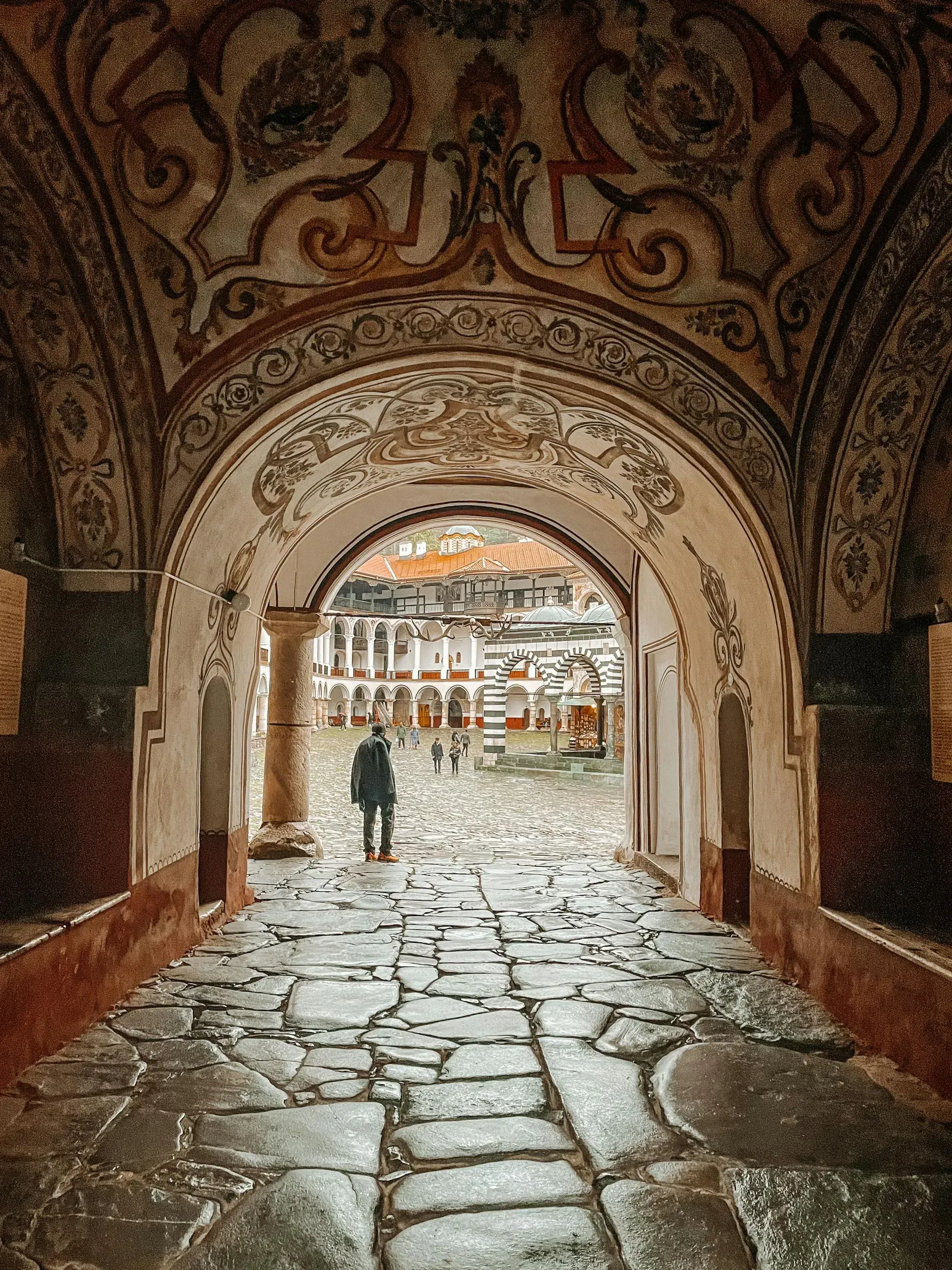 A scenic view through an arched monastery entrance leading to the courtyard of Rila Monastery, Bulgaria.