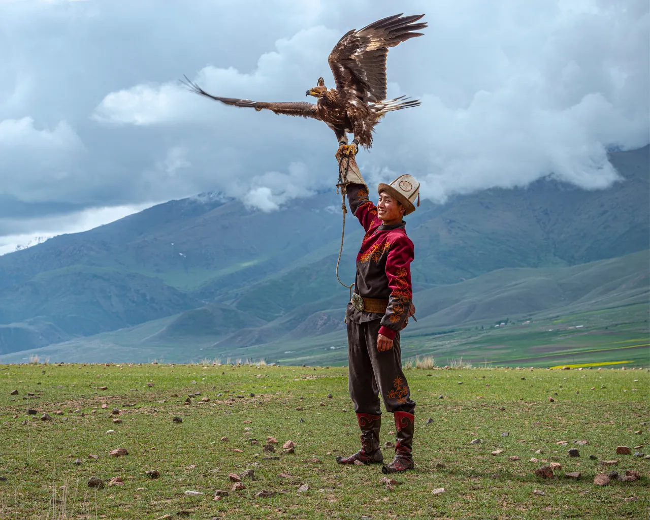 Kyrgyzstan Eagle Hunter - Kyrgyz hunter in traditional attire raising a golden eagle in an open field.