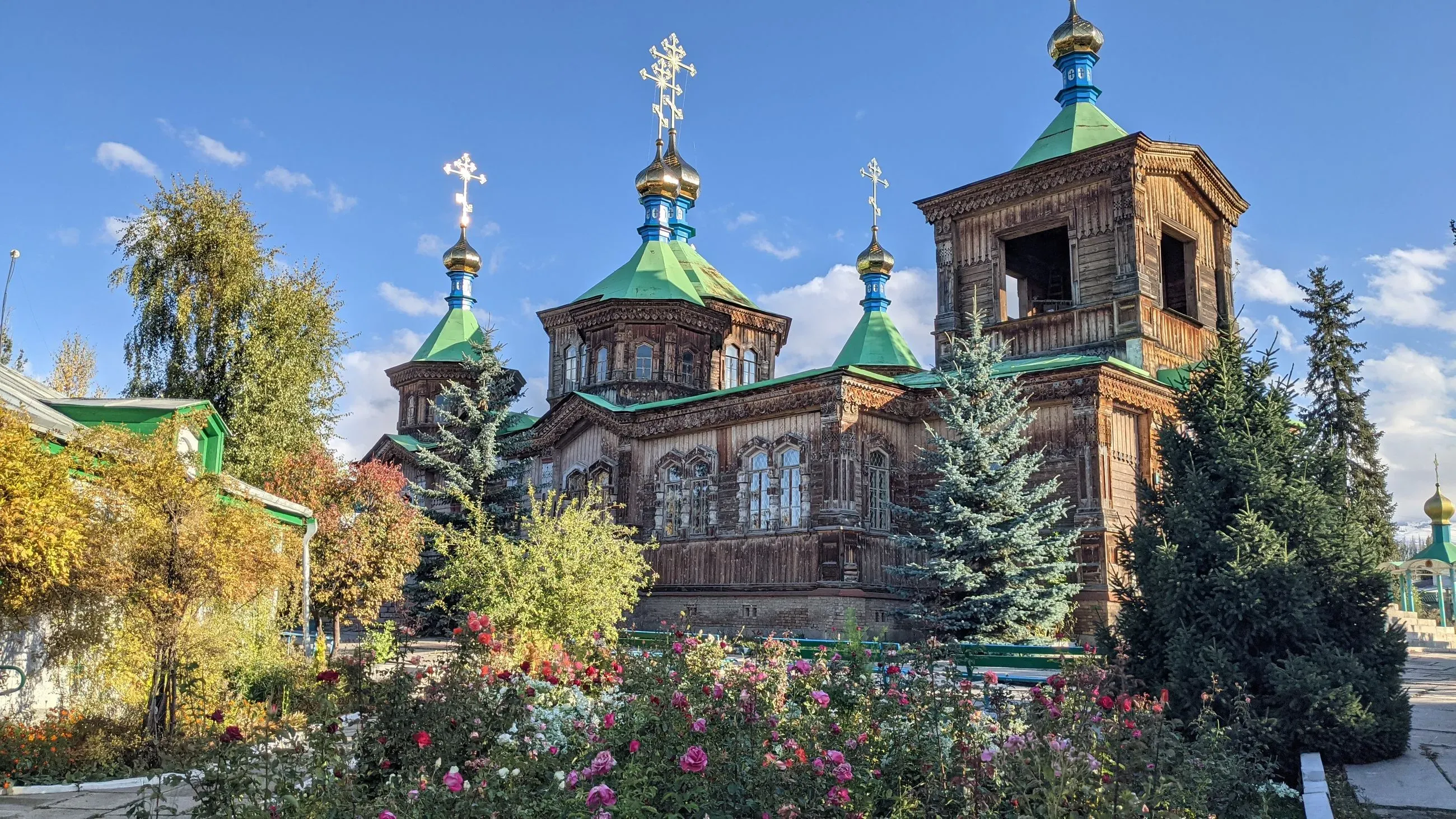 Kyrgyzstan Karakol - Ornate wooden Holy Trinity Russian Orthodox Church, framed by lush trees in Karakol, Kyrgyzstan.